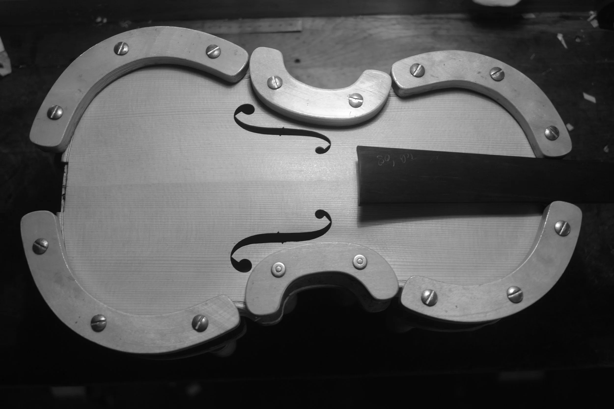 A violin-shaped game or puzzle piece with metallic edges and screws, held with a wooden handle, on a wooden surface.