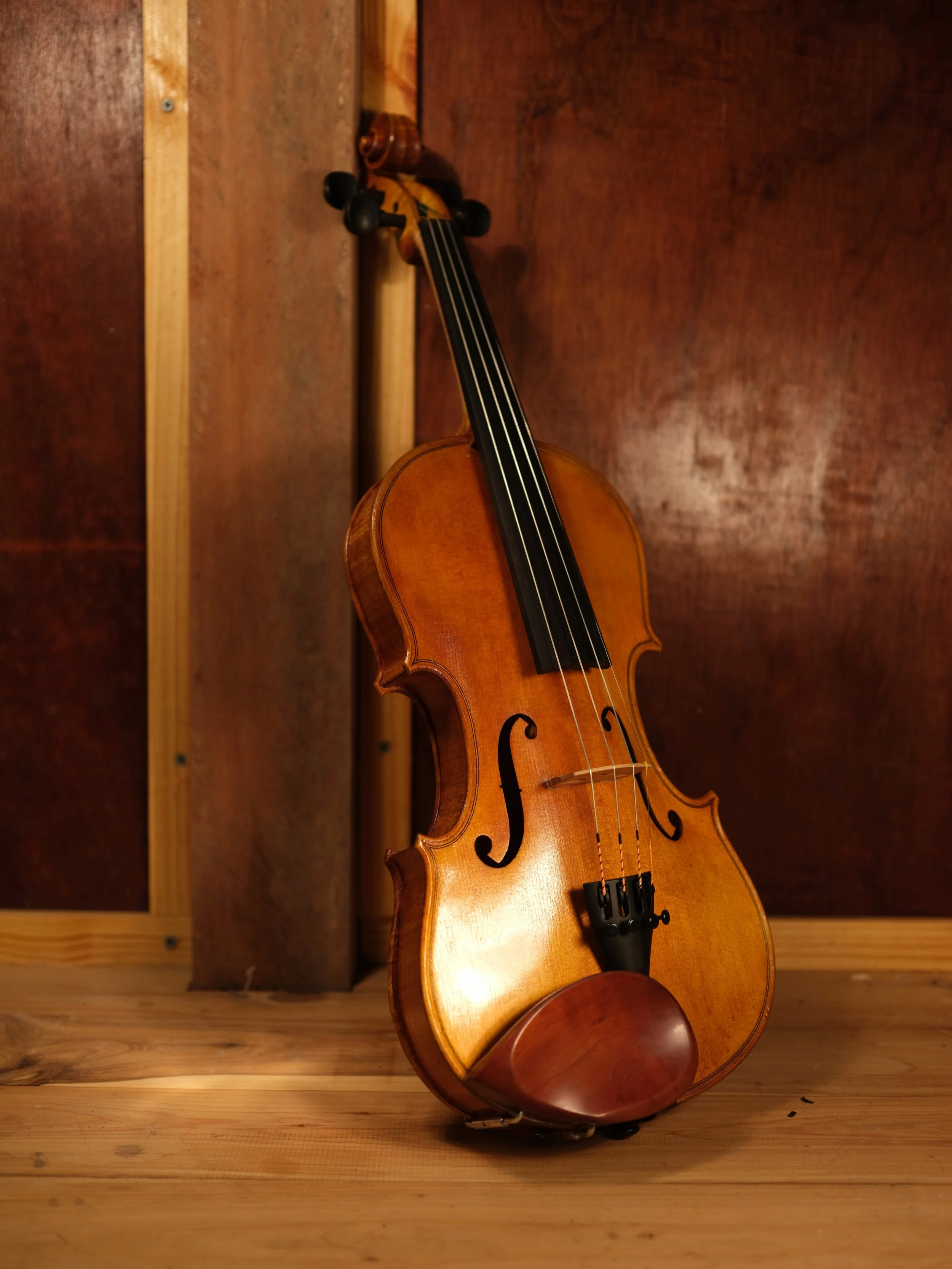 A wooden violin with a bow resting against it on a wooden surface and background.
