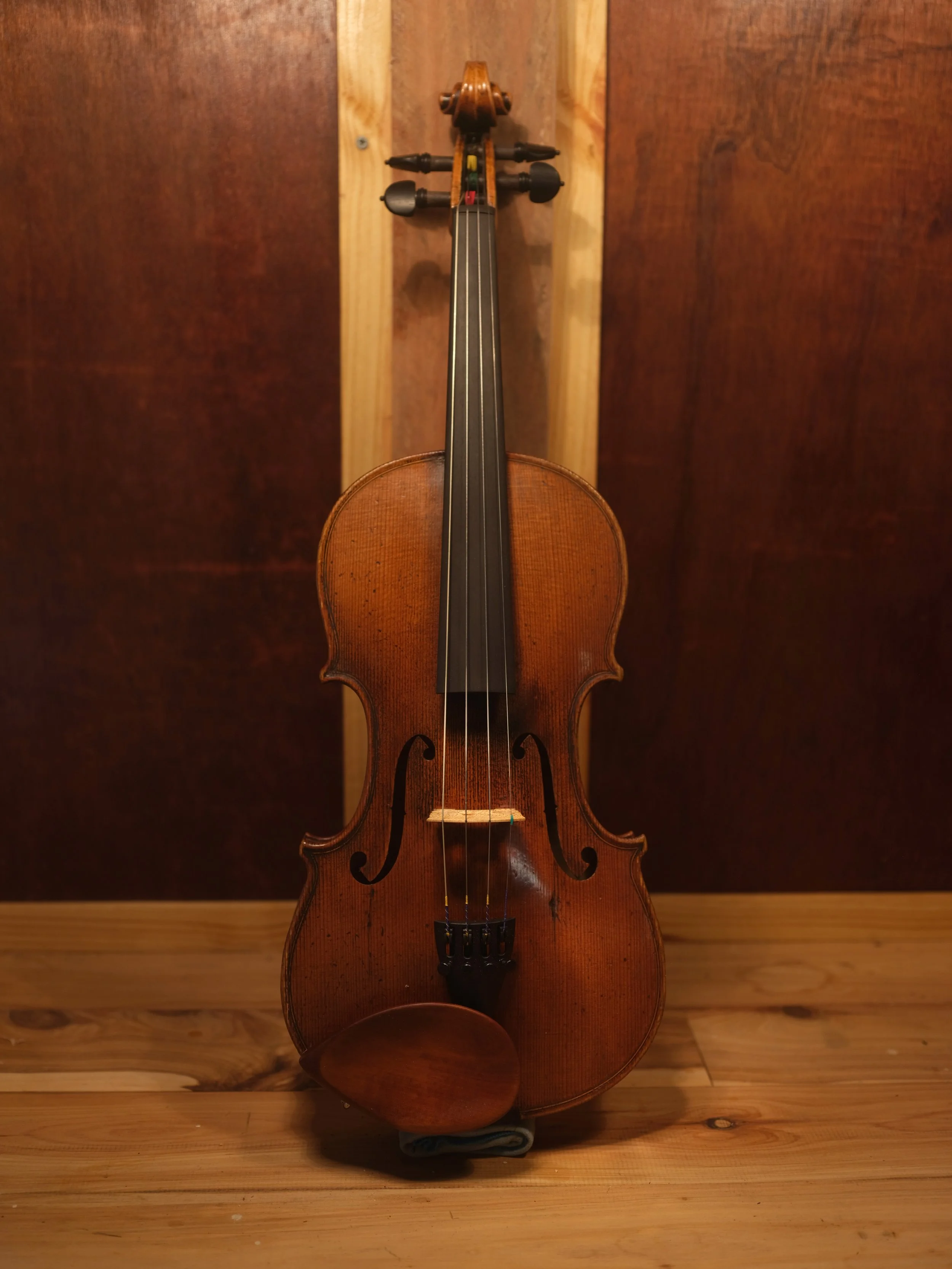 An old, wooden violin resting against a wooden wall with a wooden floor.