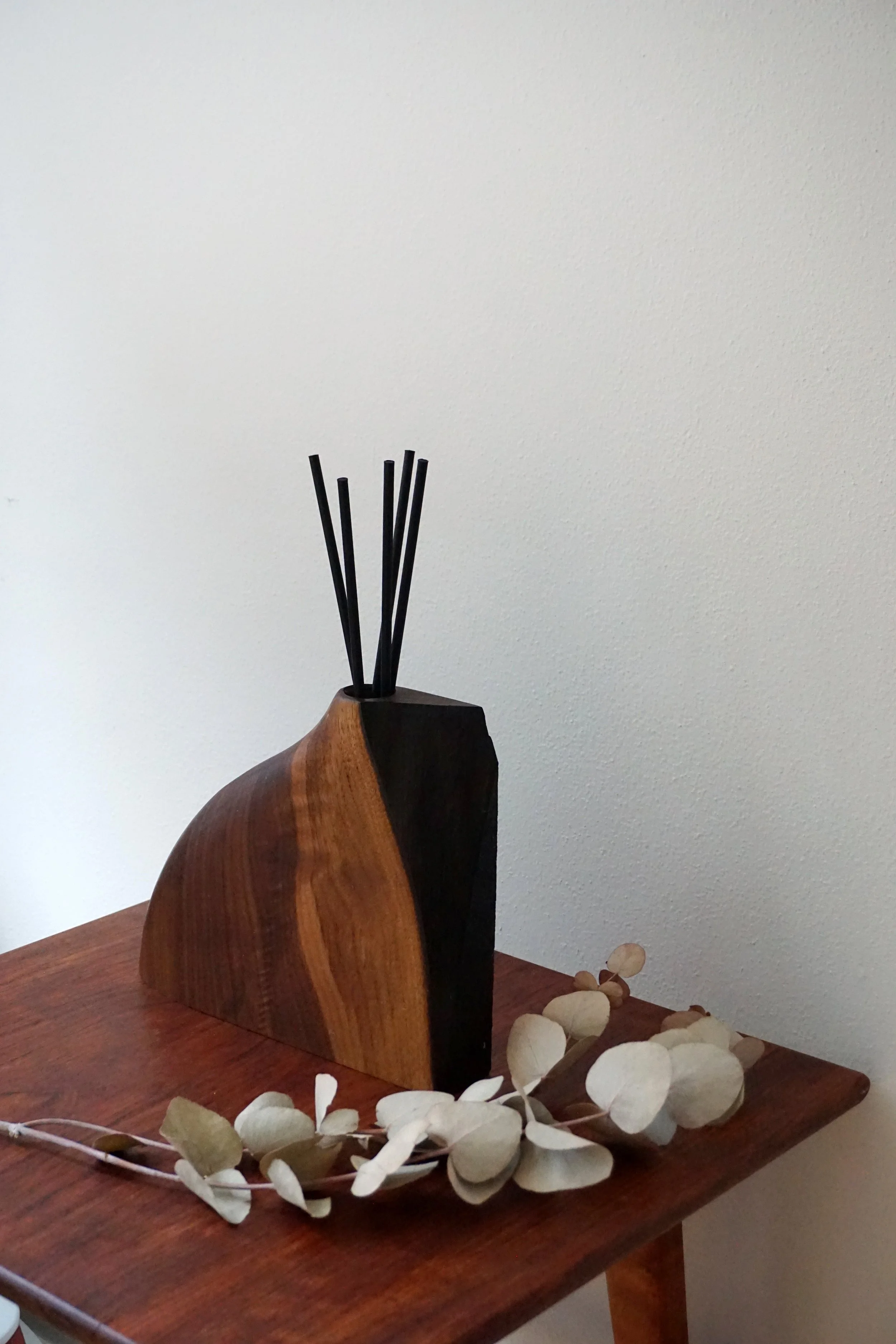 A wooden sculpture or decor piece on a table with dried white leaves around it, against a plain wall background.
