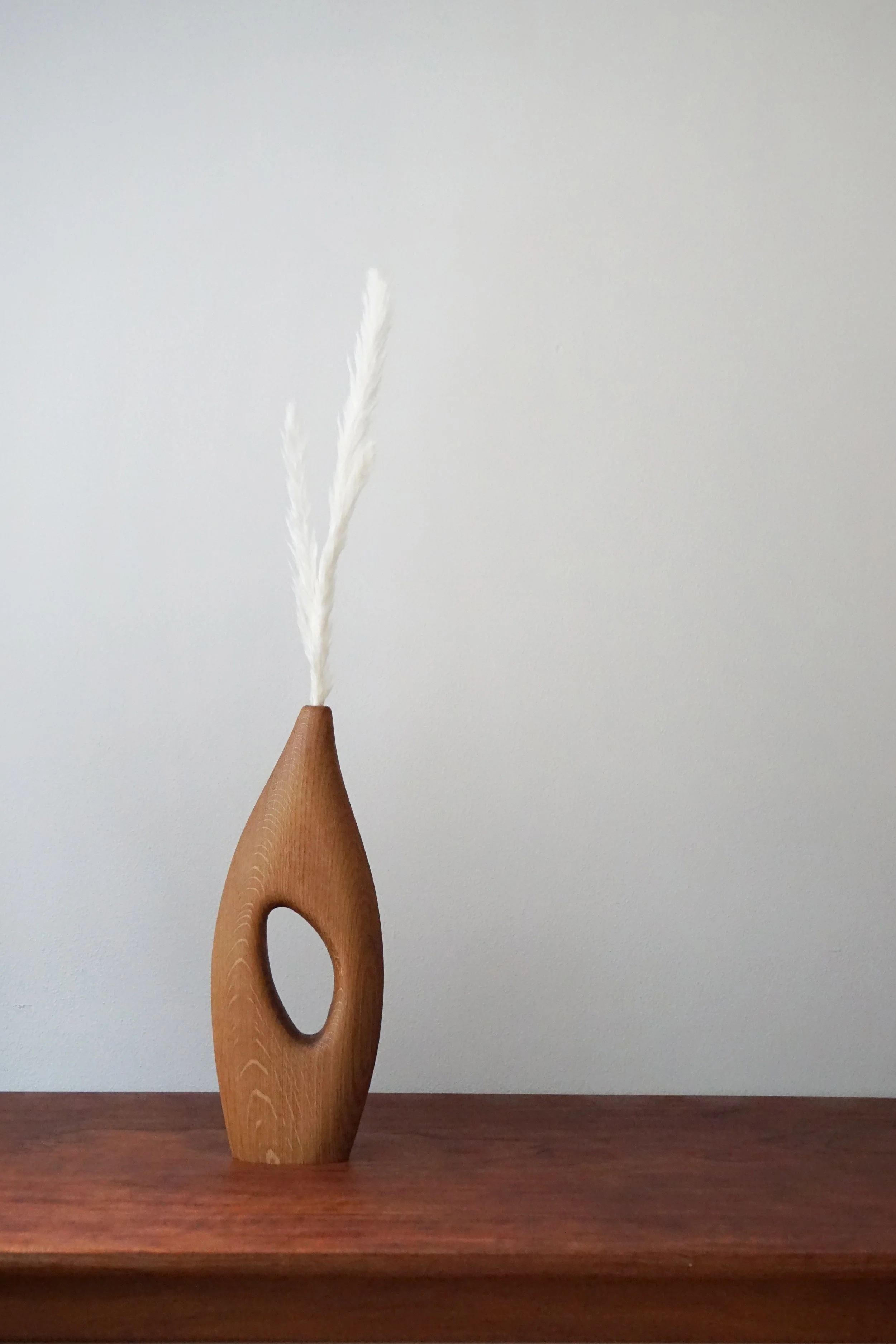 A wooden sculpture with a narrow base and an elongated hole in the middle, holding a white feather.