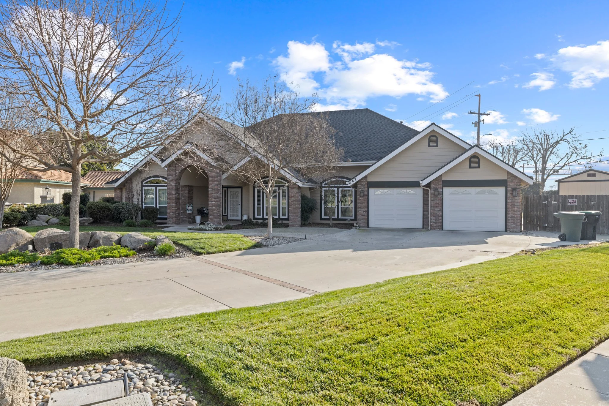 Front exterior view of a house with a lawn, trees, and a driveway, under a partly cloudy sky.