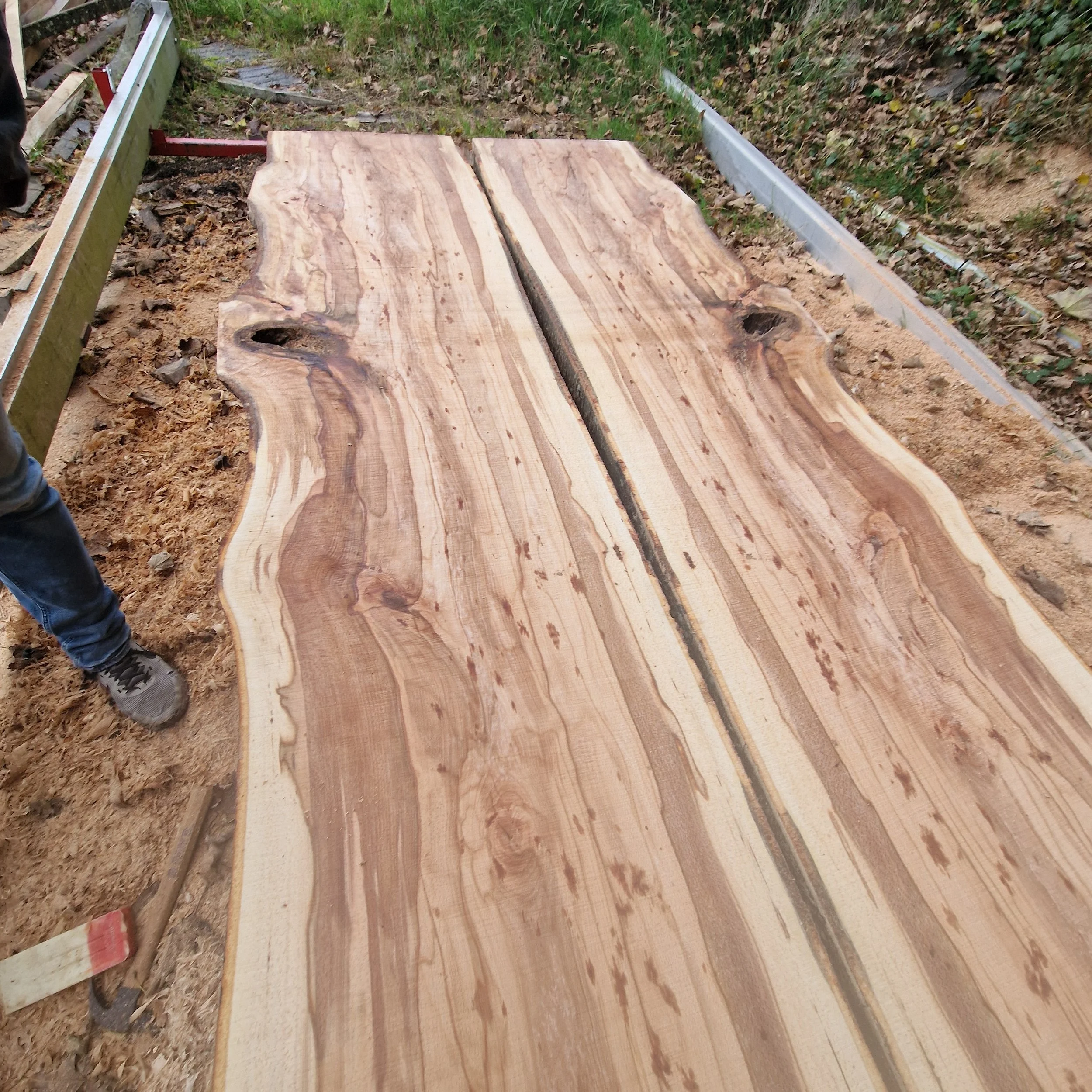 A large wooden slab with natural edges laid on the ground outdoors, surrounded by construction materials and dirt.