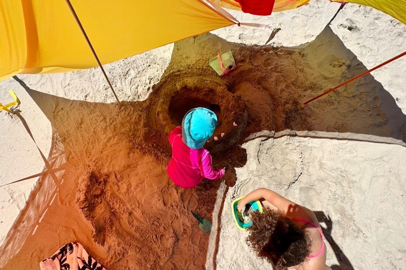 Two children the shade building a sandcastle on the beach under two Zinnia Sunshade canopies linked together.