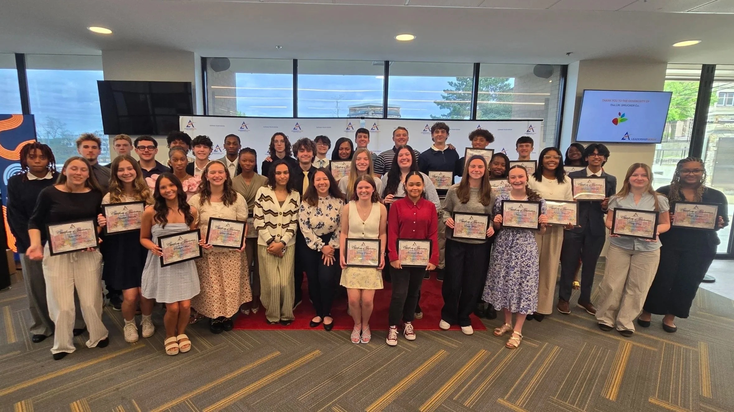 Junior Leadership Akron class of approximately 40 high school students smile towards the camera with their program completion certificates.