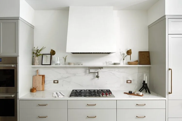 Modern kitchen with white marble backsplash, gray cabinets, and open shelf with decorative items