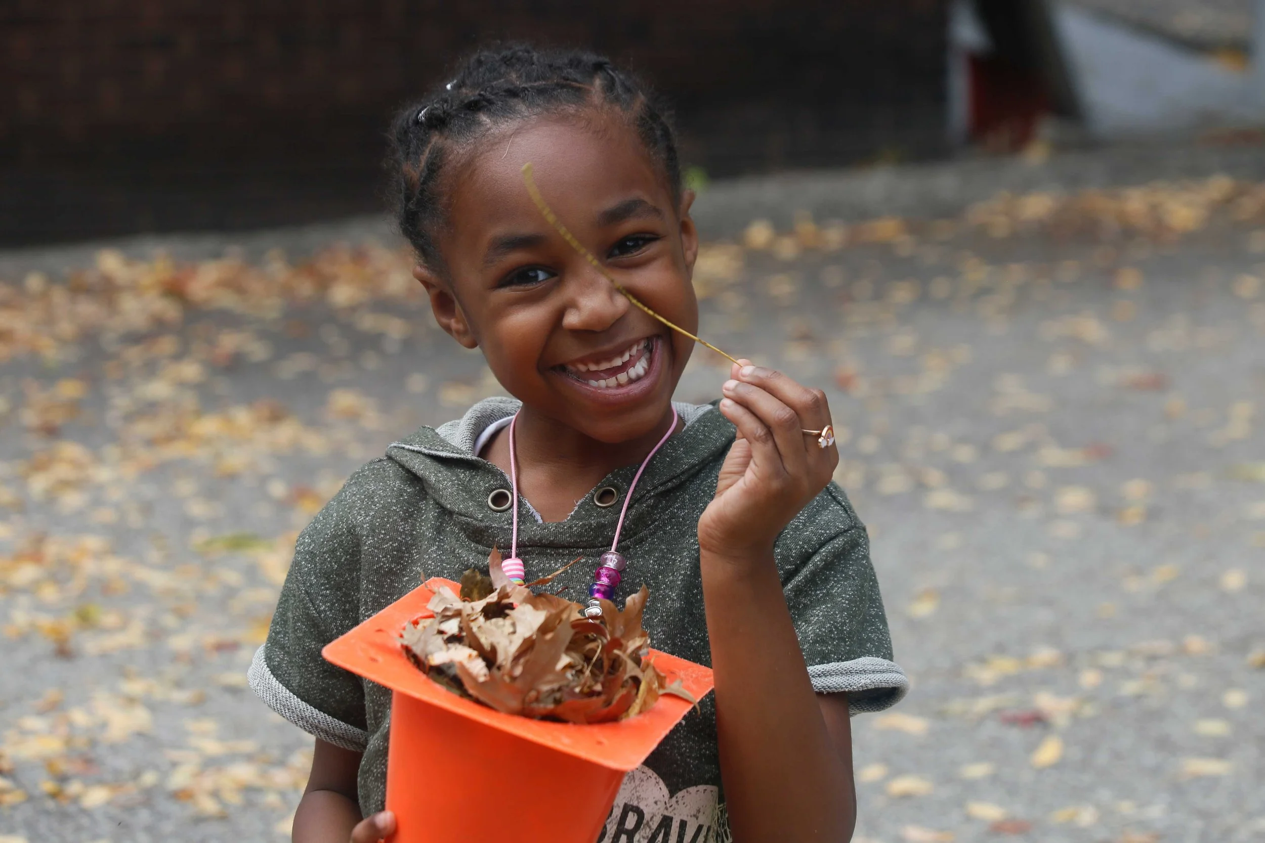 Fusion student holding a cone full of freshly fallen autumn leaves while smiling