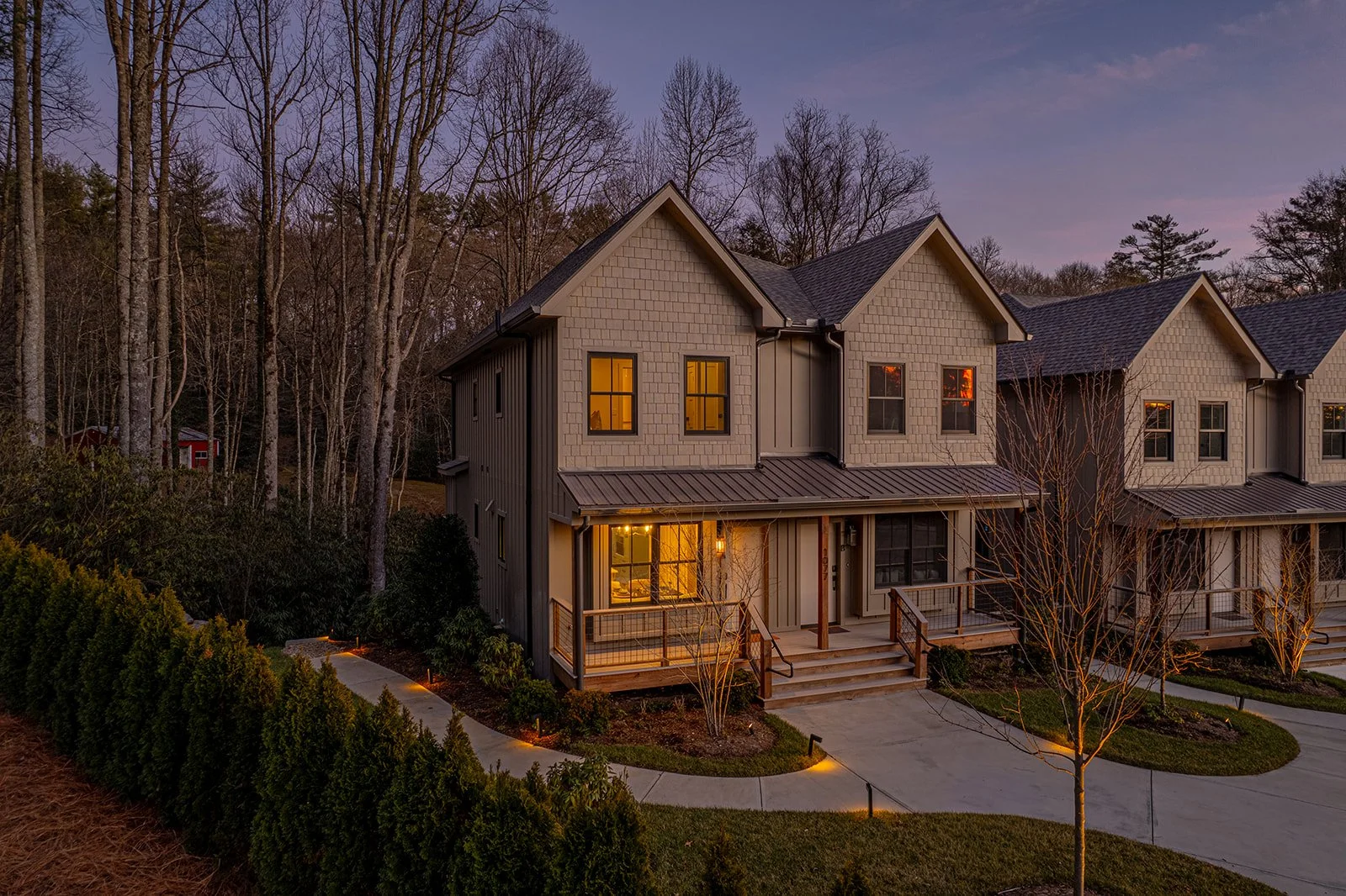Modern townhouse with exterior lighting at dusk, surrounded by trees and shrubs.
