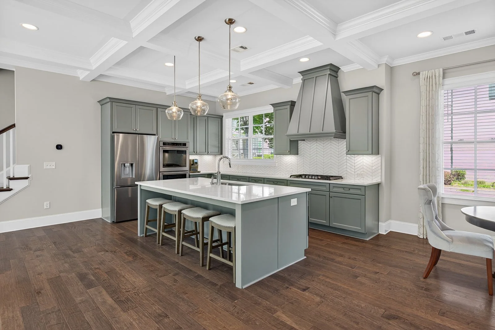 Modern kitchen with gray cabinets, white island with seating, stainless steel refrigerator, and pendant lighting.