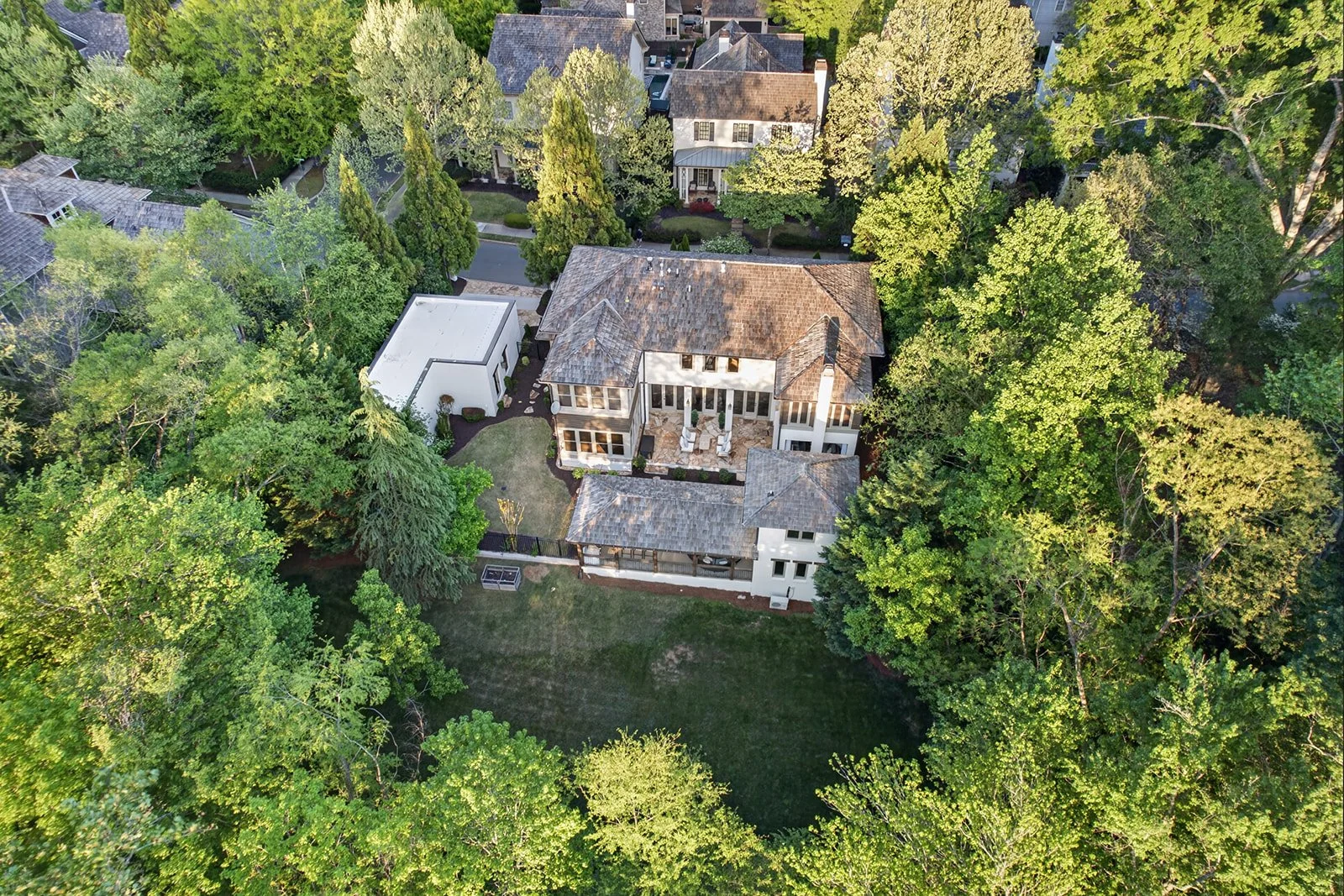An aerial view of a large house surrounded by trees and greenery in a neighborhood.