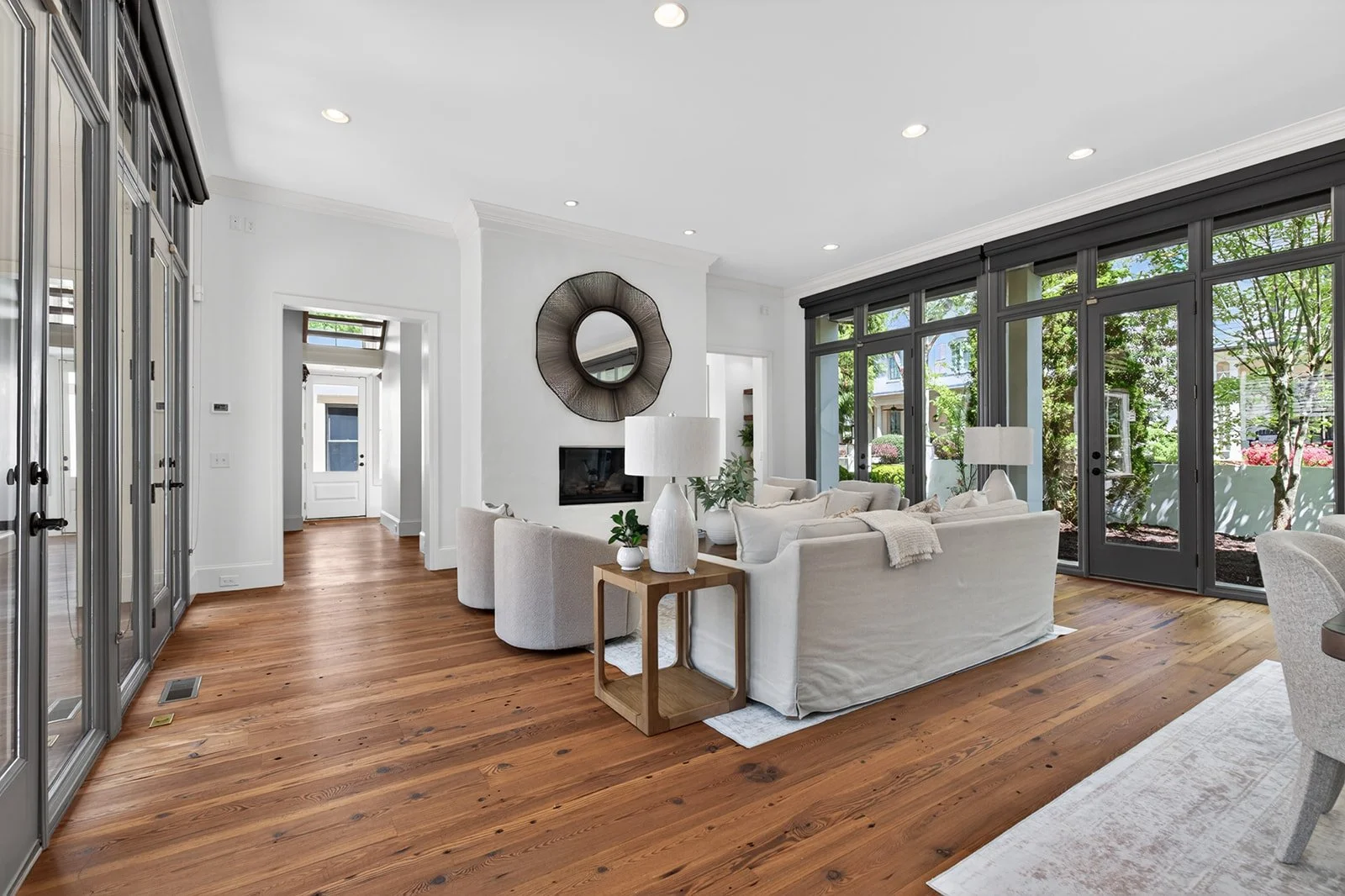 Living room with wooden floors, white couches, large windows, and a door leading outside.