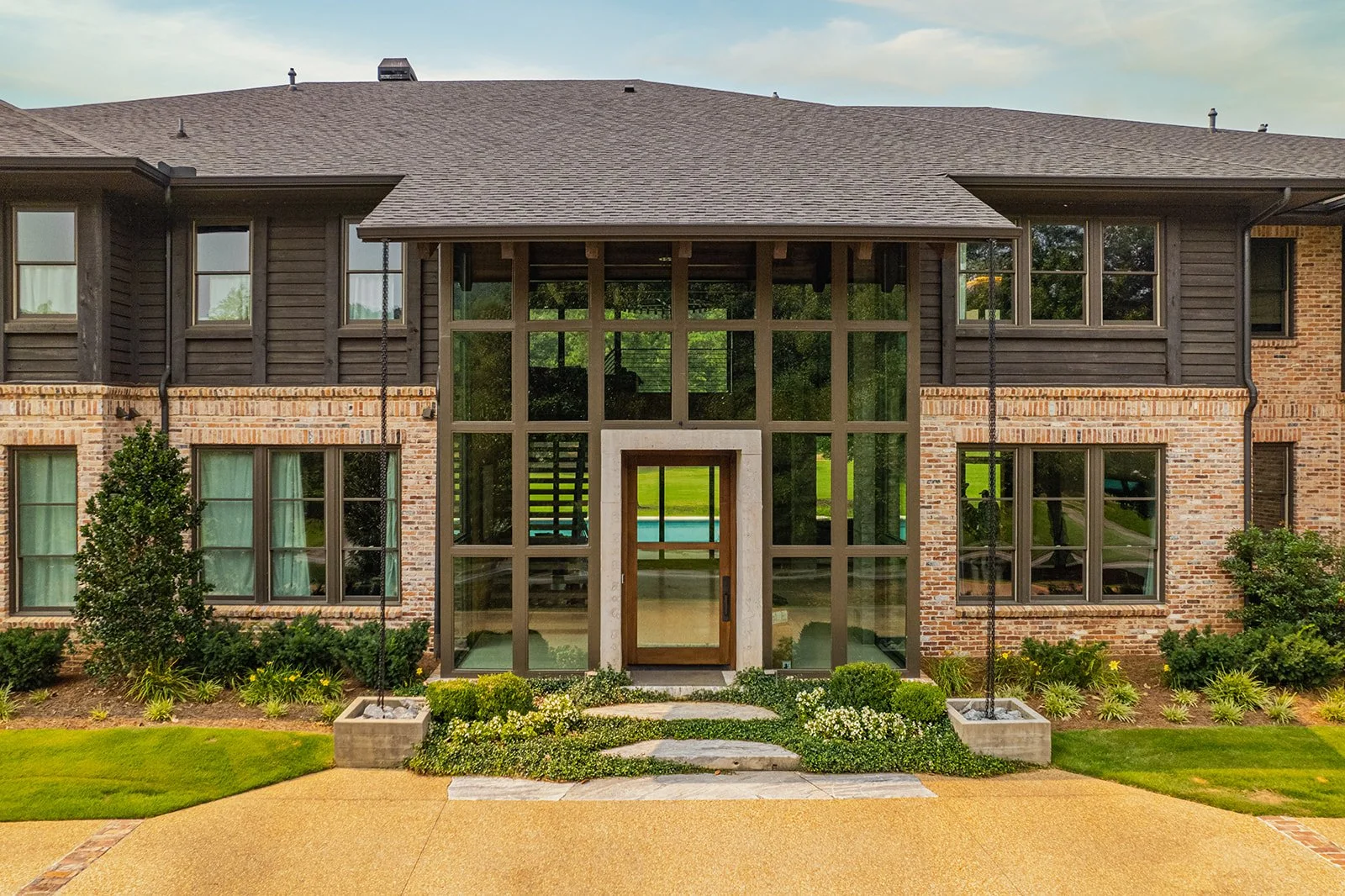 Front view of a modern two-story house with a brick and black wooden exterior, large glass windows, and a small porch with a landscaped garden in front.