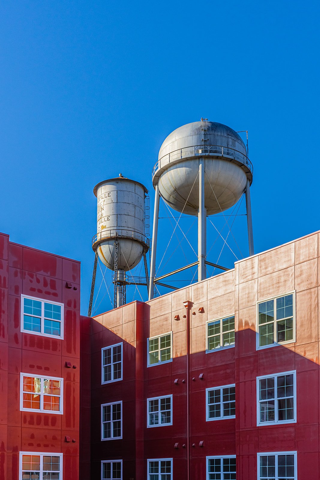 Red building with multiple windows and two water towers on the roof under a clear blue sky.