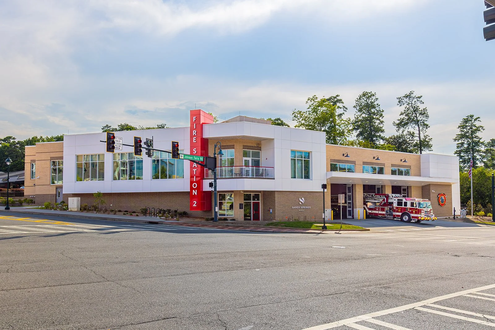 Fire station building with a red firefighter emblem, a fire truck parked outside, and traffic lights at an intersection on Johnson Ferry Road in Sandy Springs.