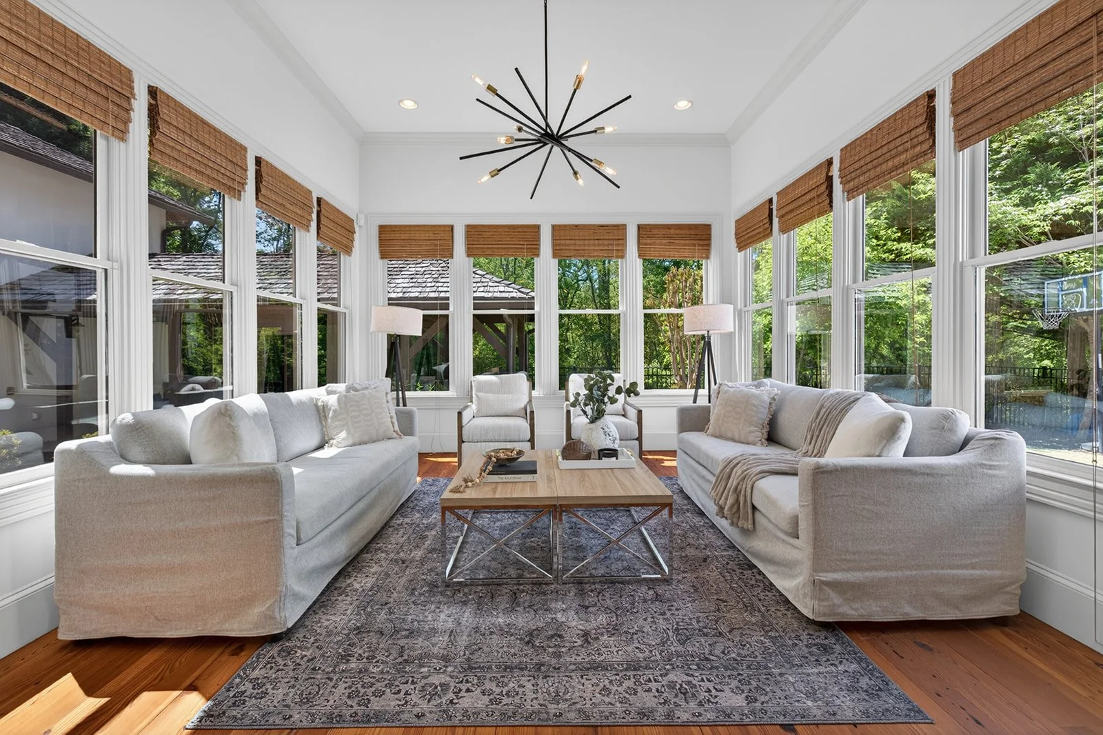 Bright living room with large windows, white sofas, wooden coffee table, area rug, and modern ceiling light fixture.