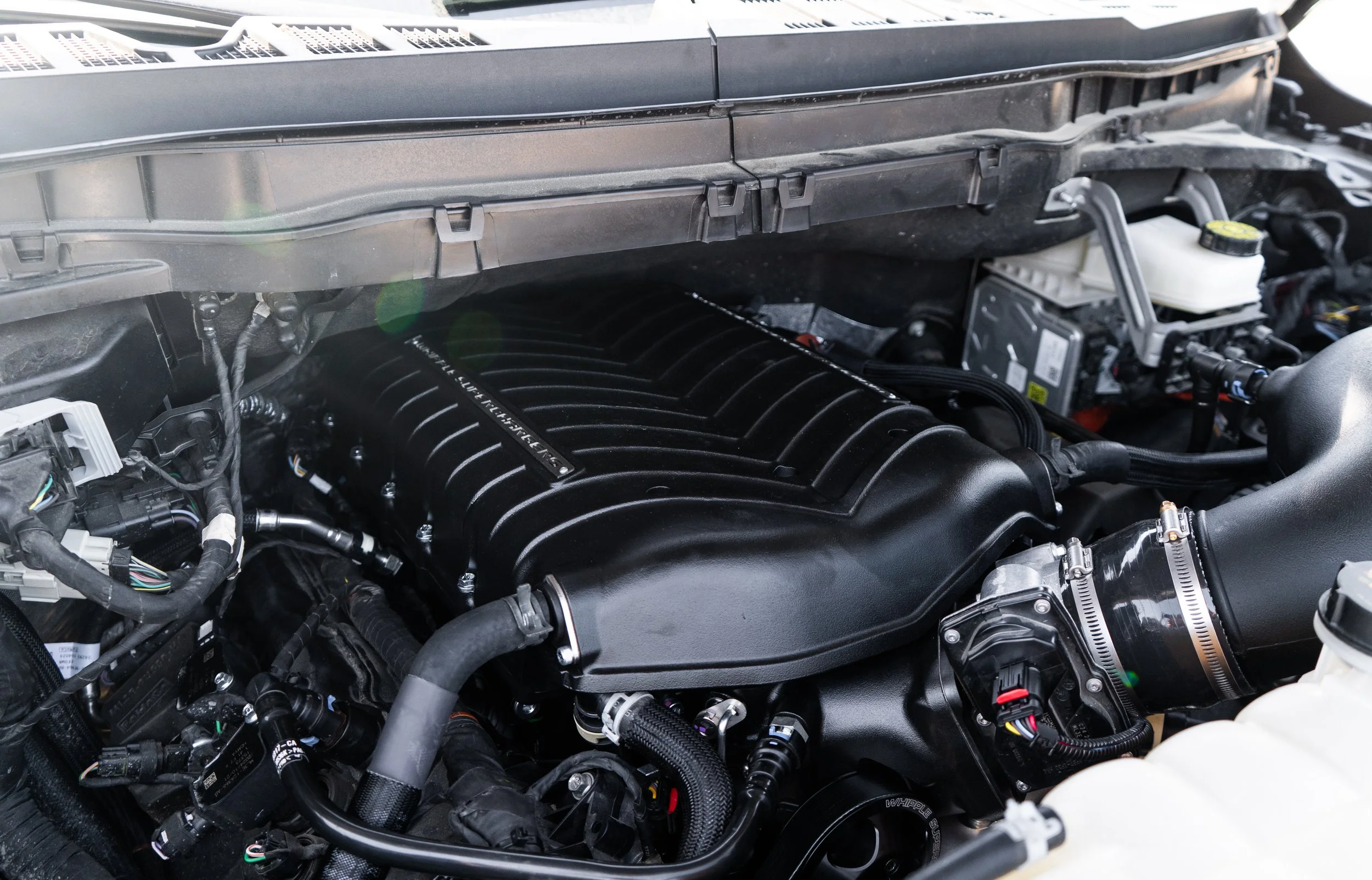 Close-up of a sports car engine through a rear window, with visible red 'Corvette' branding on the engine cover.