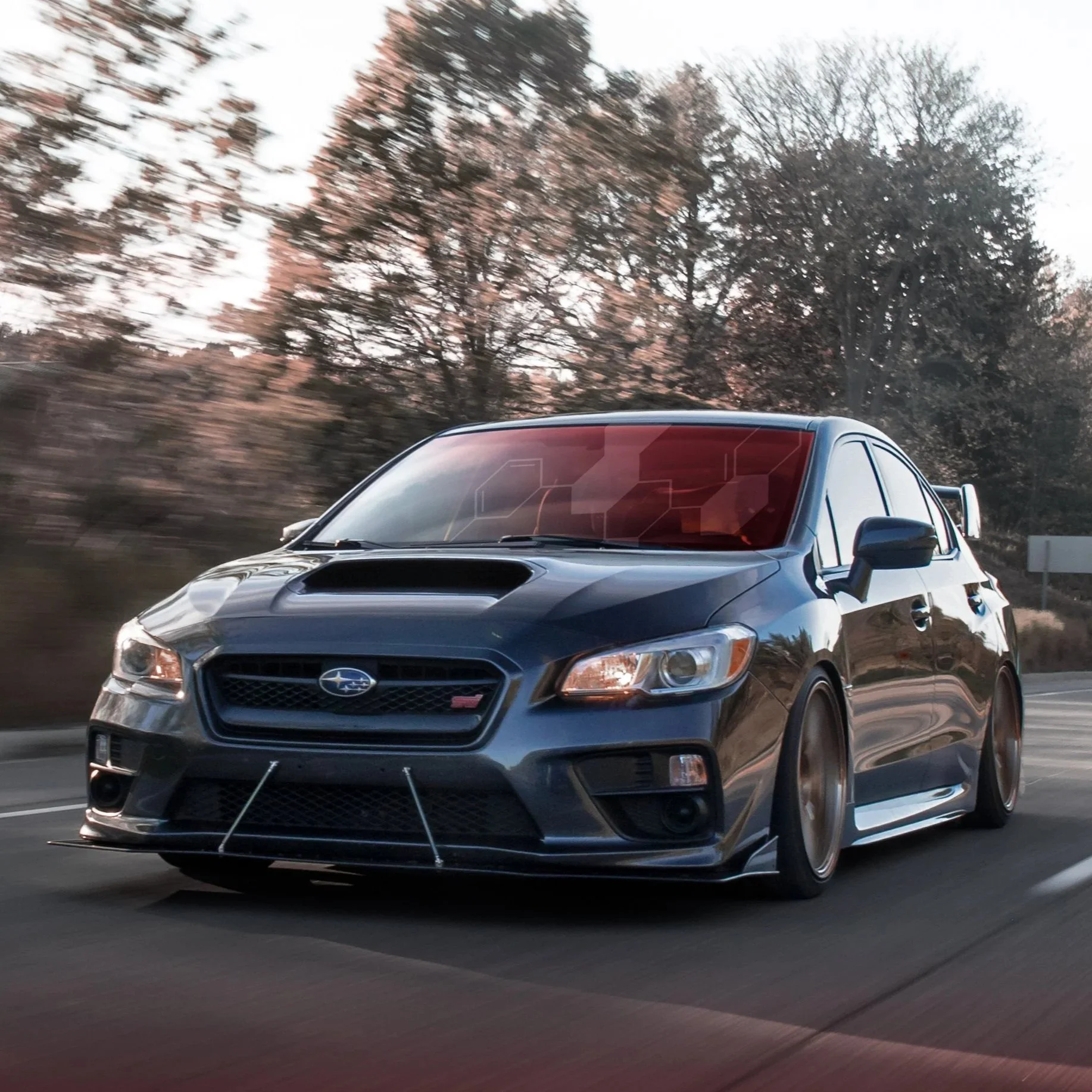 A black Subaru WRX driving on a highway with trees in the background.