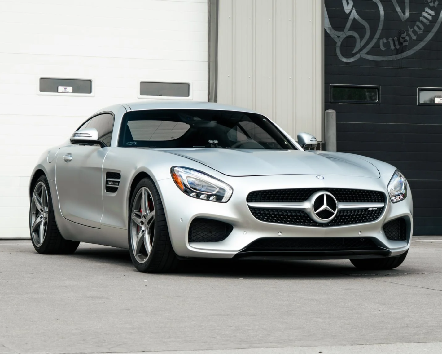 Front view of a black luxury BMW car parked on an empty asphalt lot with trees and a partly cloudy sky in the background.