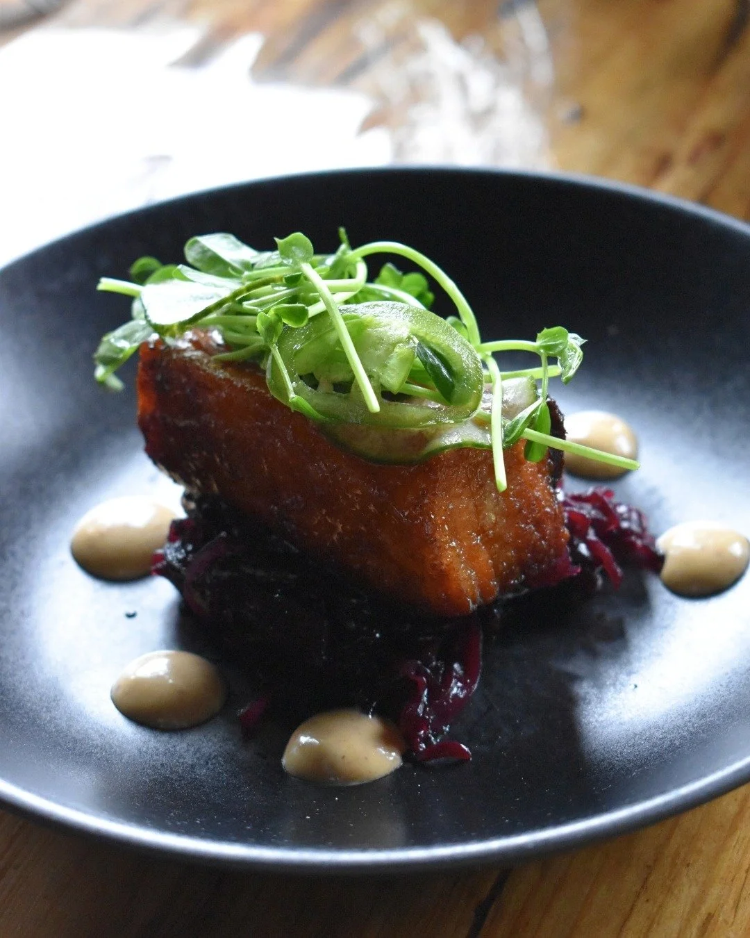 Crisp pork belly meets tangy braised cabbage, sweet maple glaze, and chipotle aioli&mdash;balanced with a garden-fresh microgreen salad.🌿