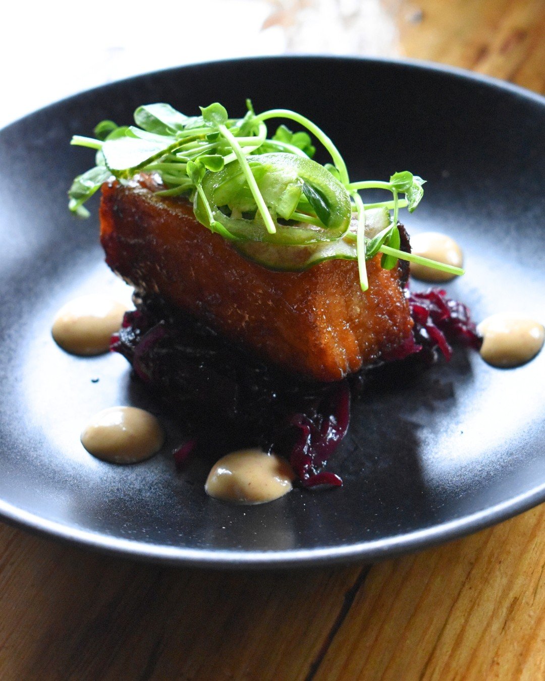 A layered plate of maple-kissed pork belly, warm braised cabbage, and chipotle heat🌿🔥