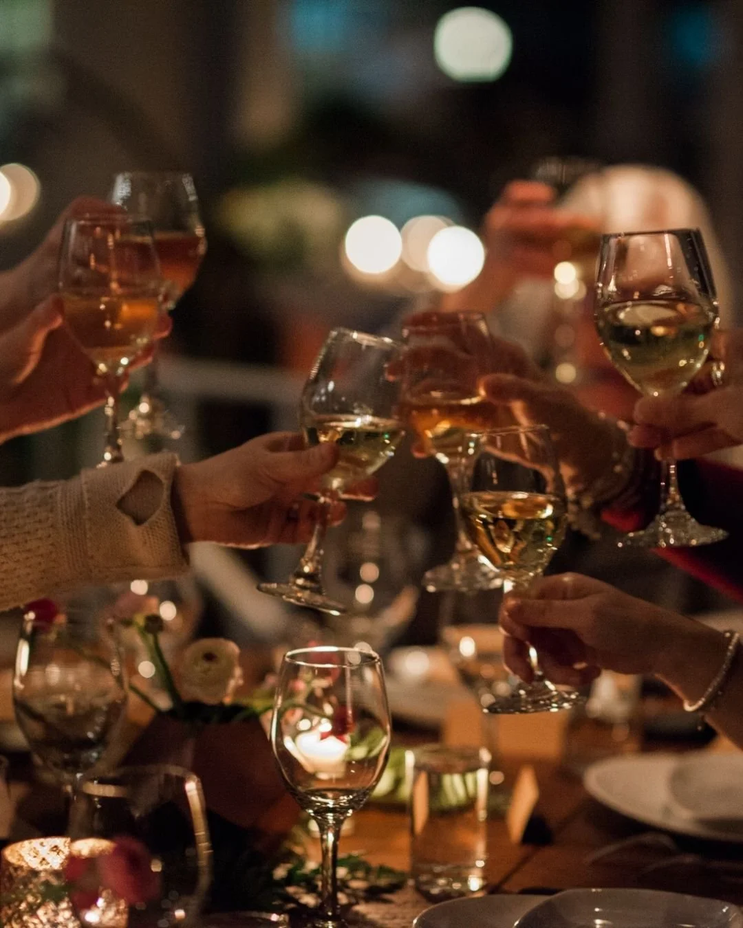People toasting with glasses of white wine at a dinner party in a warmly lit setting.