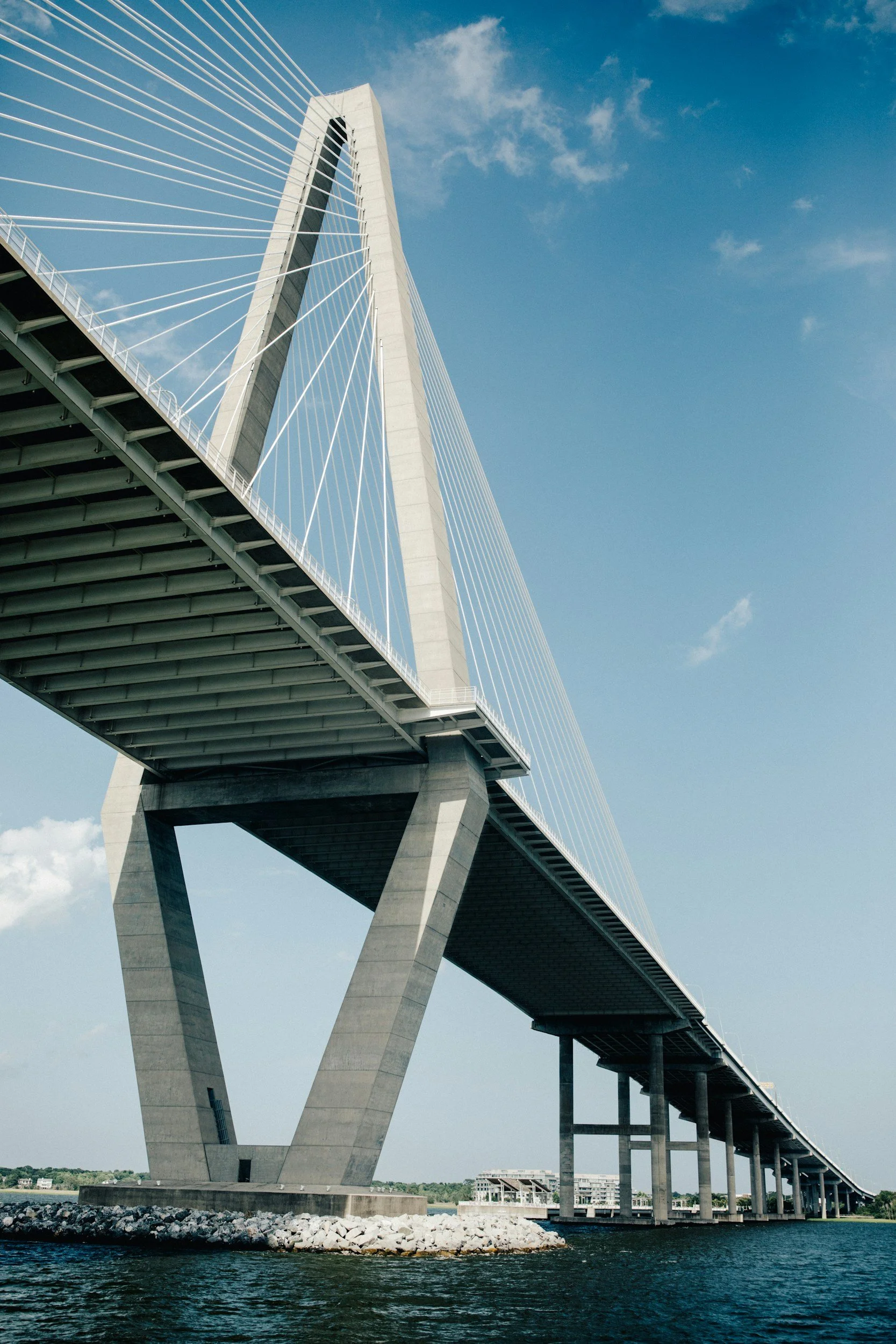 A large modern cable-stayed bridge with a prominent central tower, spanning over a body of water under a partly cloudy blue sky.
