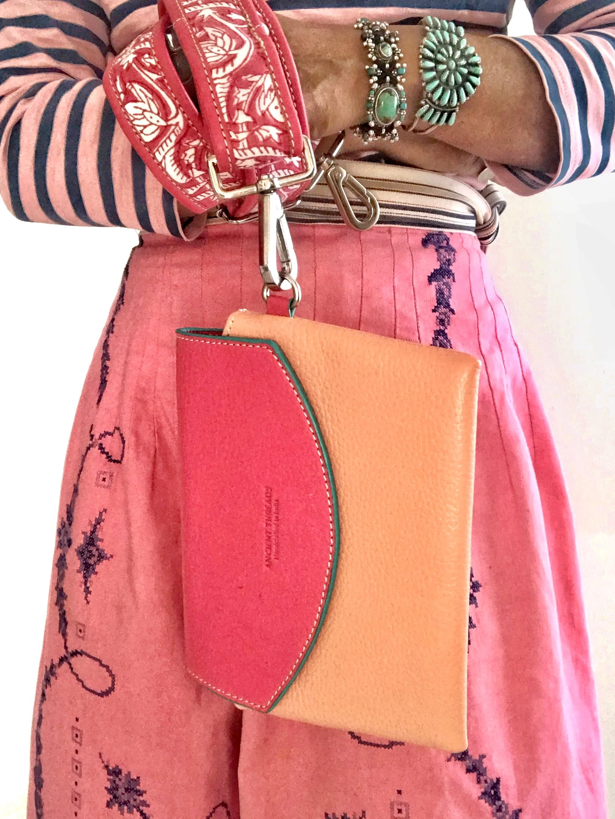 A pink embroidered skirt with a striped long-sleeve shirt, accessorized with turquoise jewelry, a red patterned purse, and a multicolored wallet.
