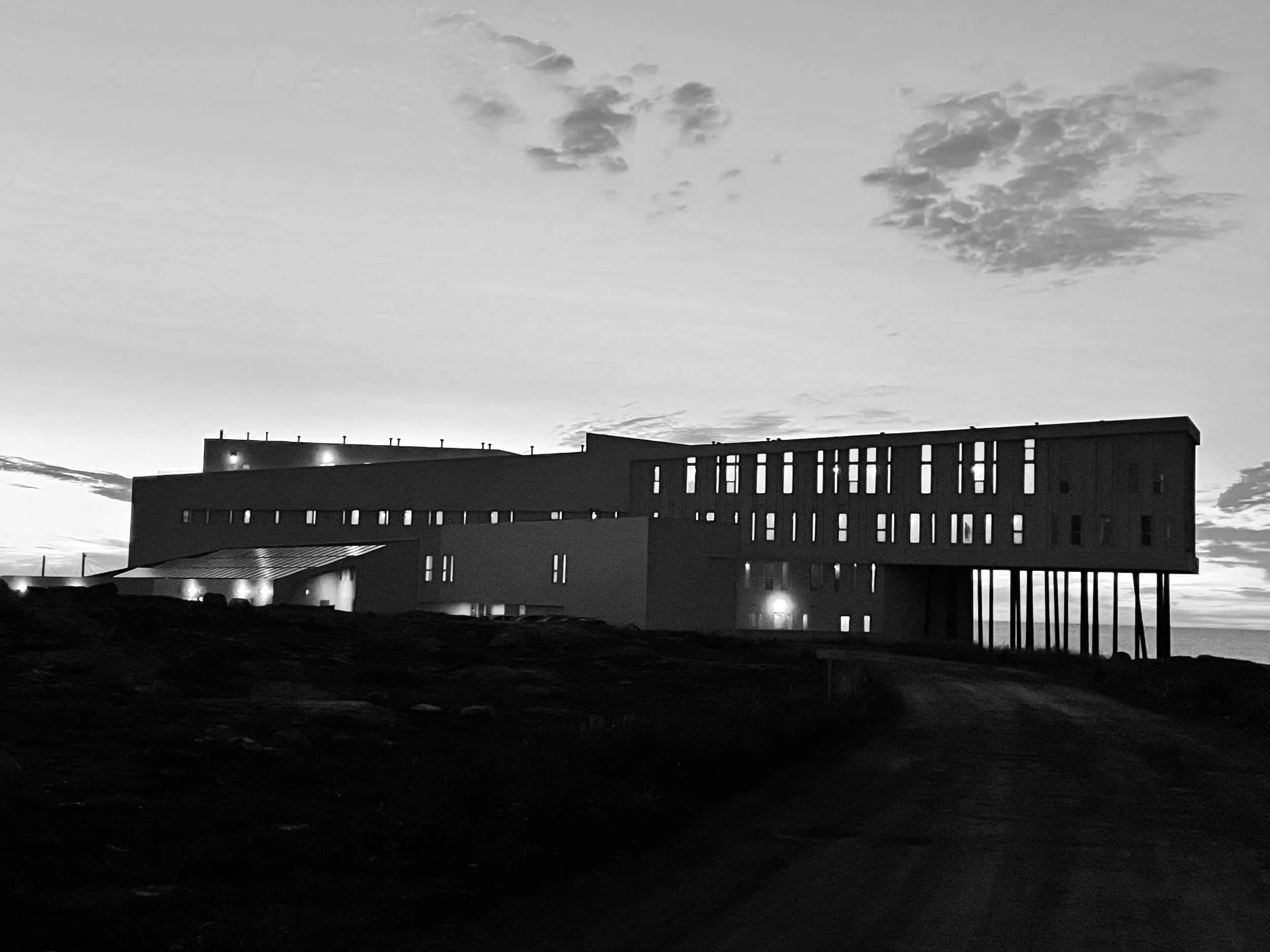 Bâtiment moderne sur pilotis au coucher du soleil, en noir et blanc.