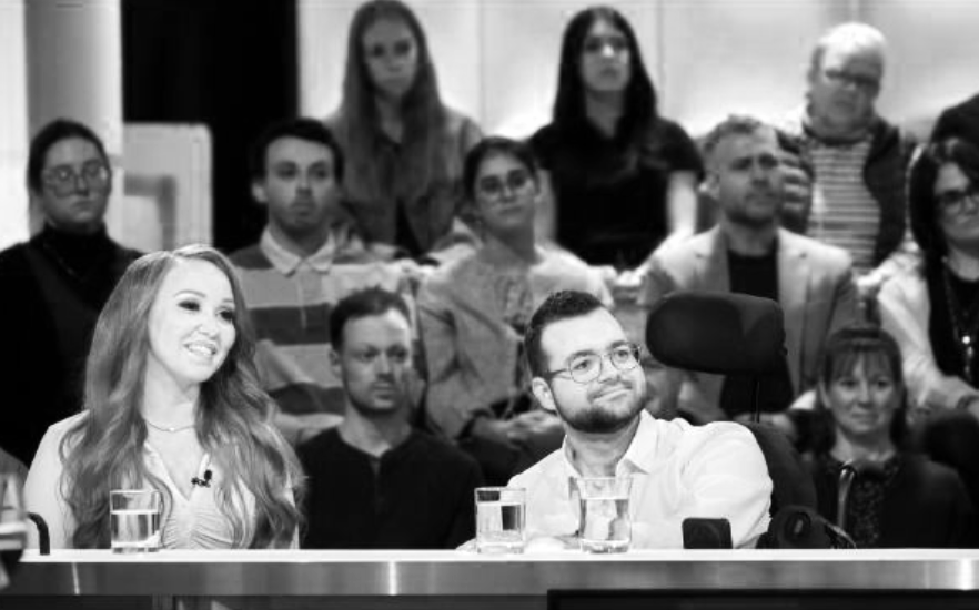 Groupe de personnes assises dans une salle, certains souriants, en noir et blanc.
