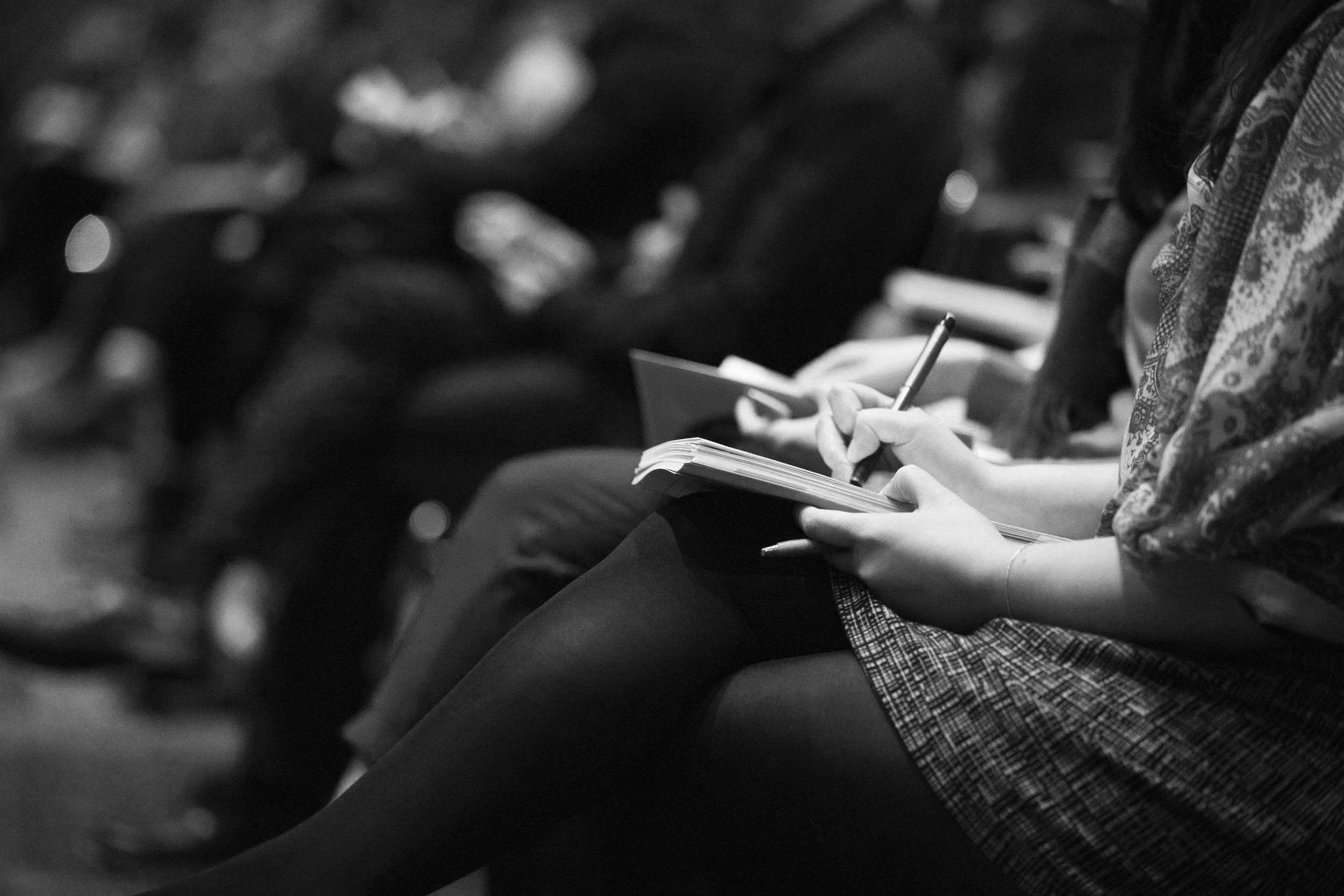  Des personnes assises en ligne, en train de prendre des notes dans un cahier. 
