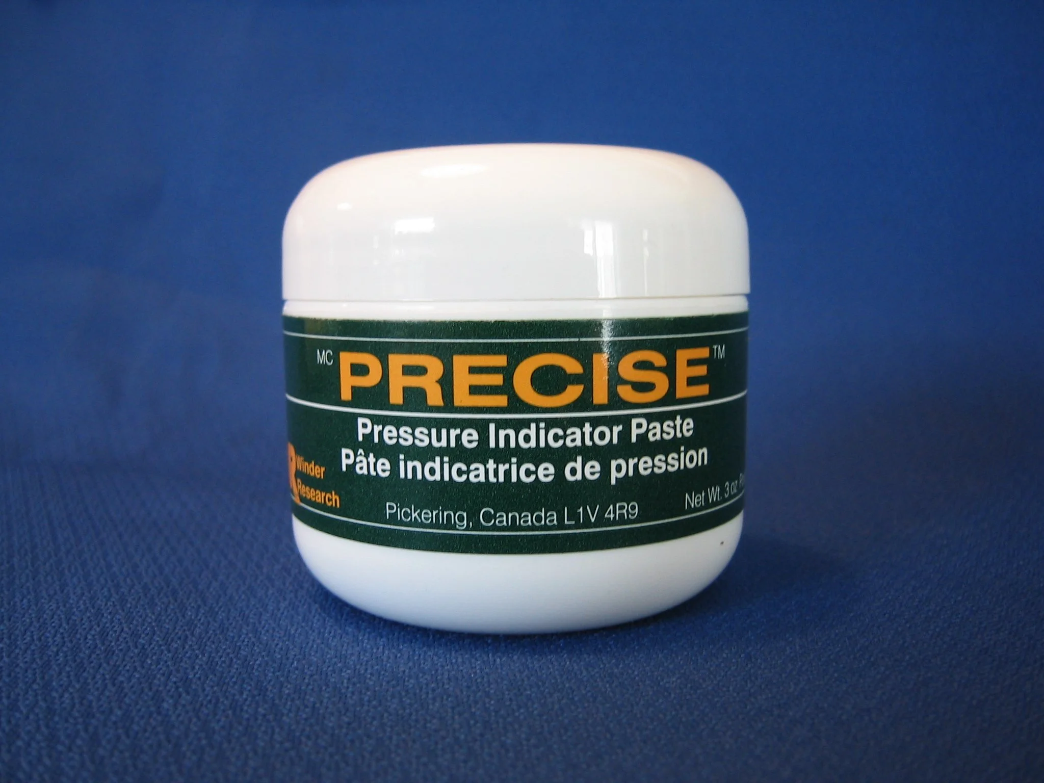 A white container labeled "PRECISE Pressure Indicator Paste" on a blue background.