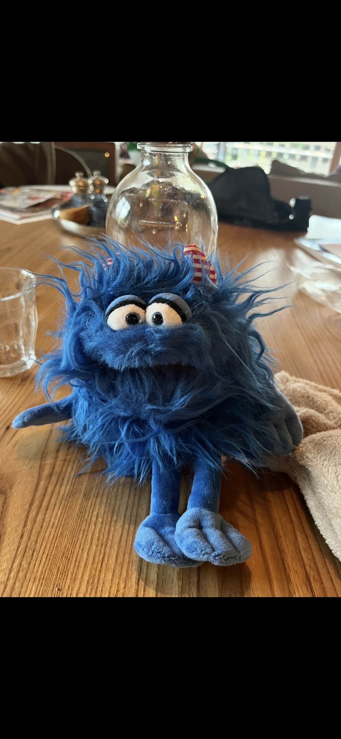 Ein Plüschtier in Form eines blauen Monster mit großen Augen, langem Fell und ausgestreckten Armen, auf einem Holztisch.