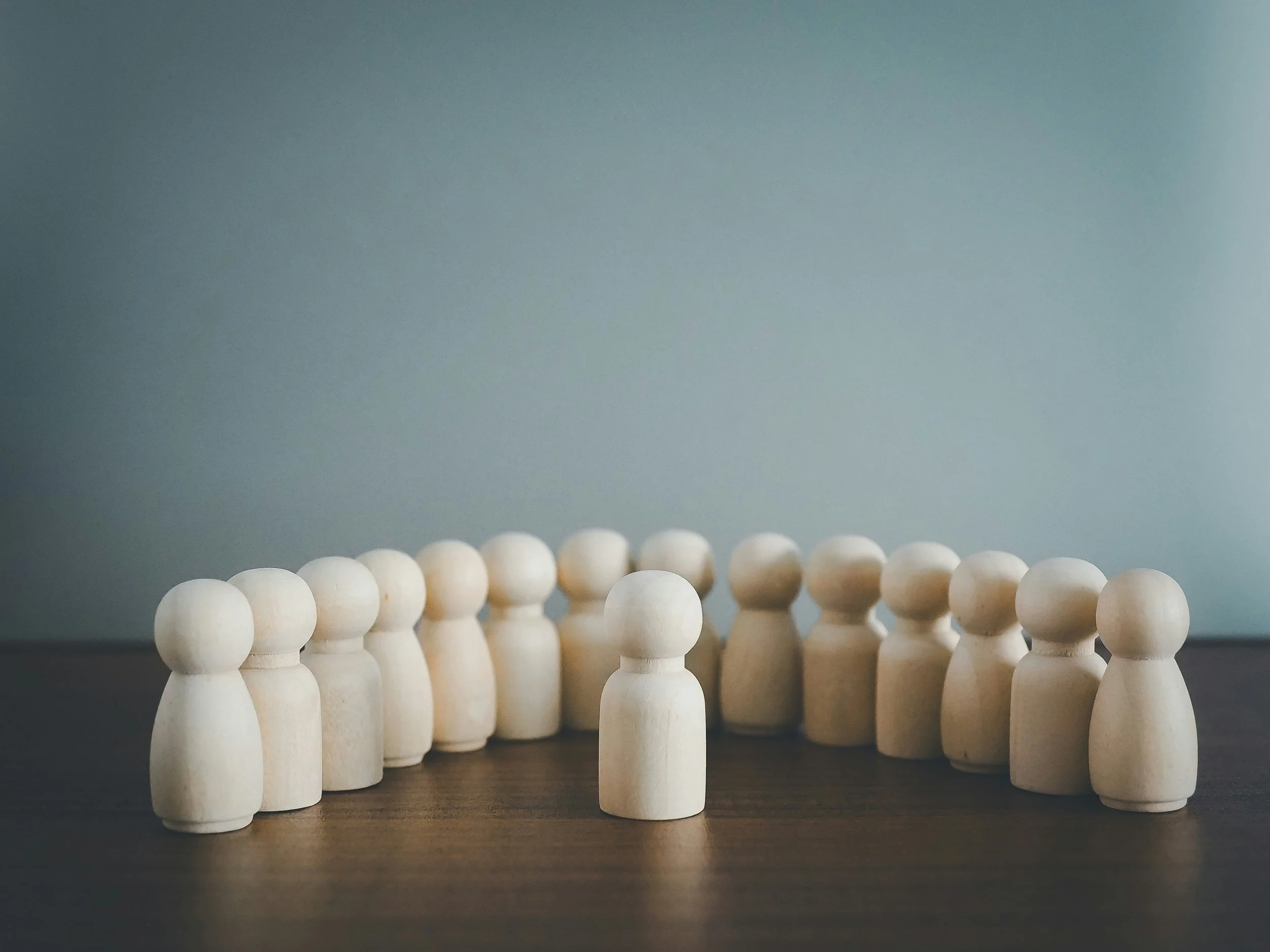 Mehrere kleine, weiße, holzene Figuren stehen in einem Kreis auf einem dunklen Tisch.