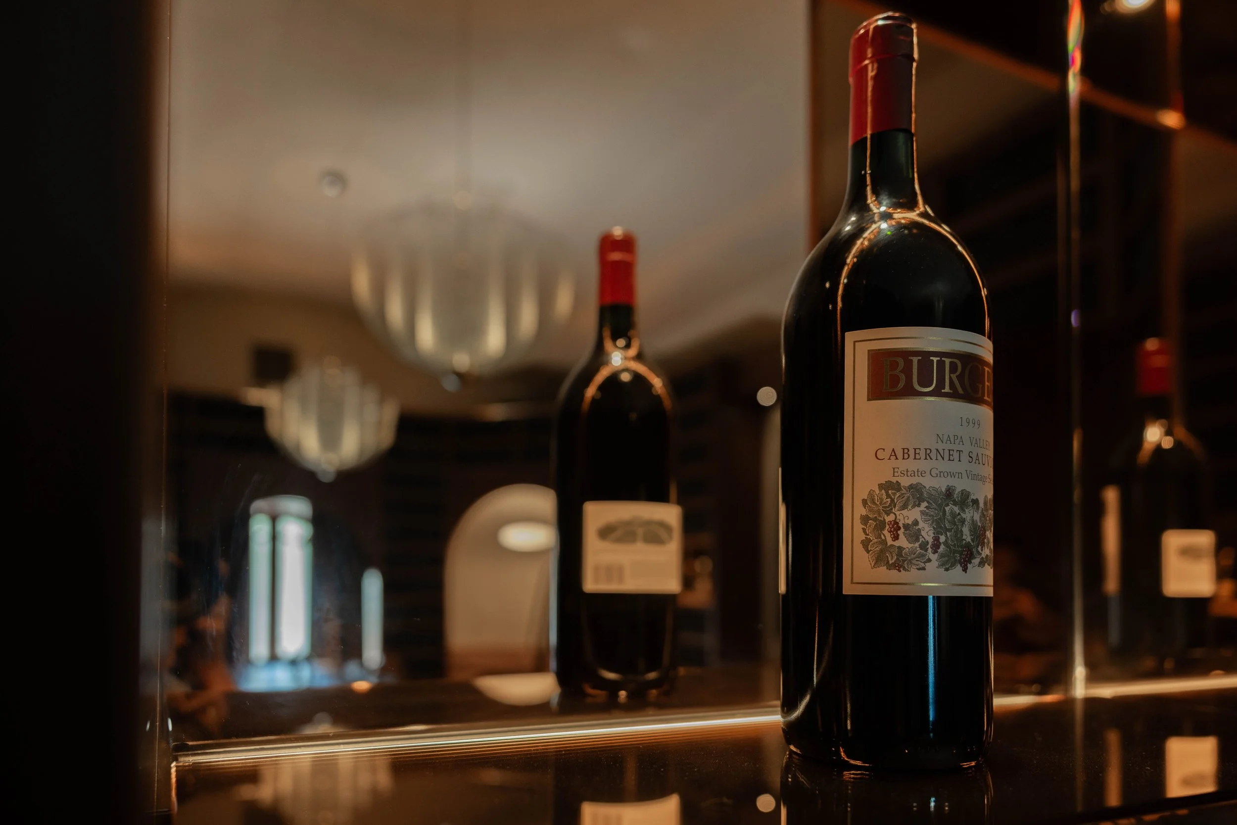 A bottle of red wine labeled 'Burg' in a wine shop, with wine glasses and other bottles in the background.