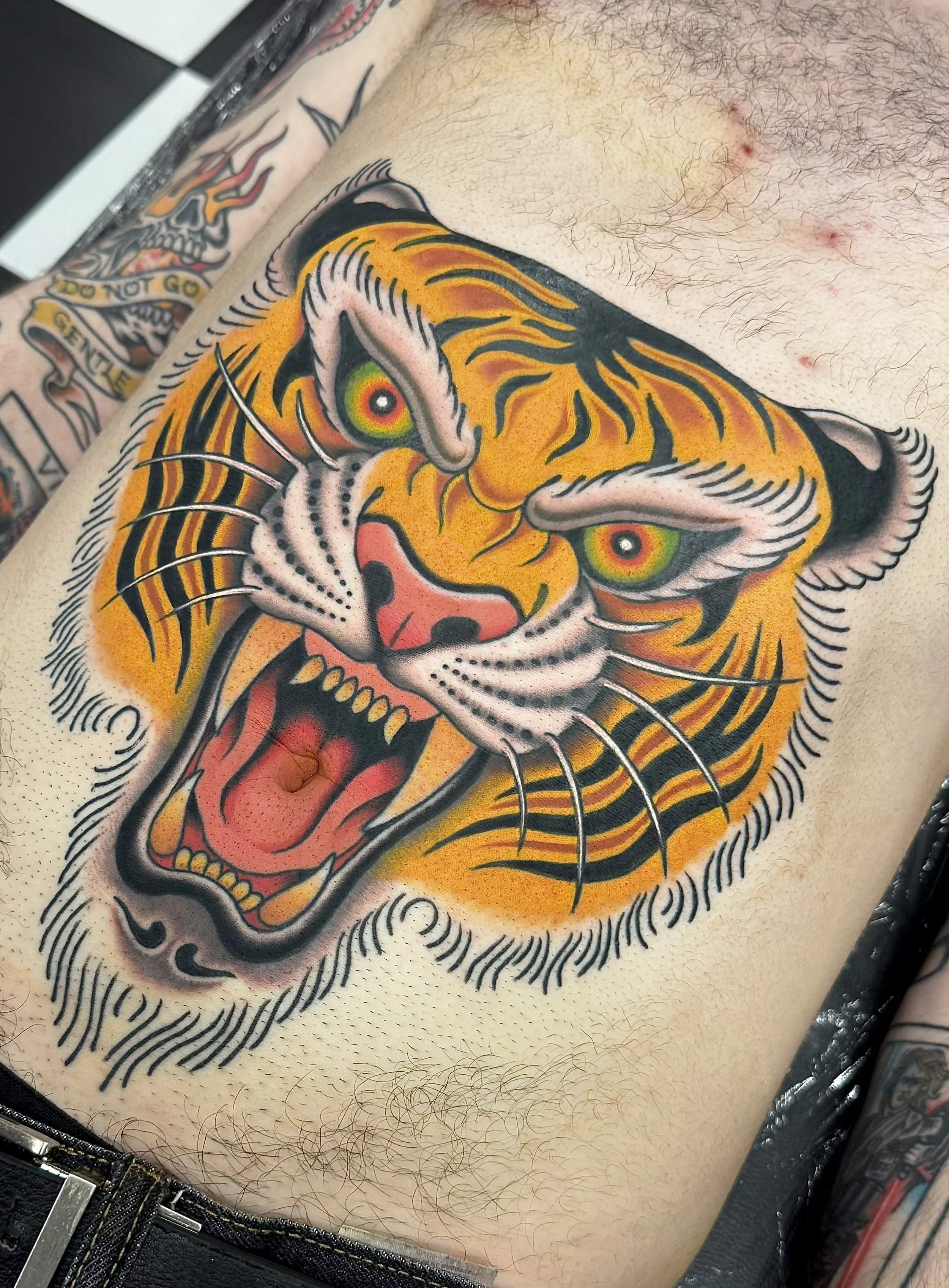 Colorful tiger tattoo on a person's chest, featuring an open mouth, detailed stripes, and piercing eyes.
