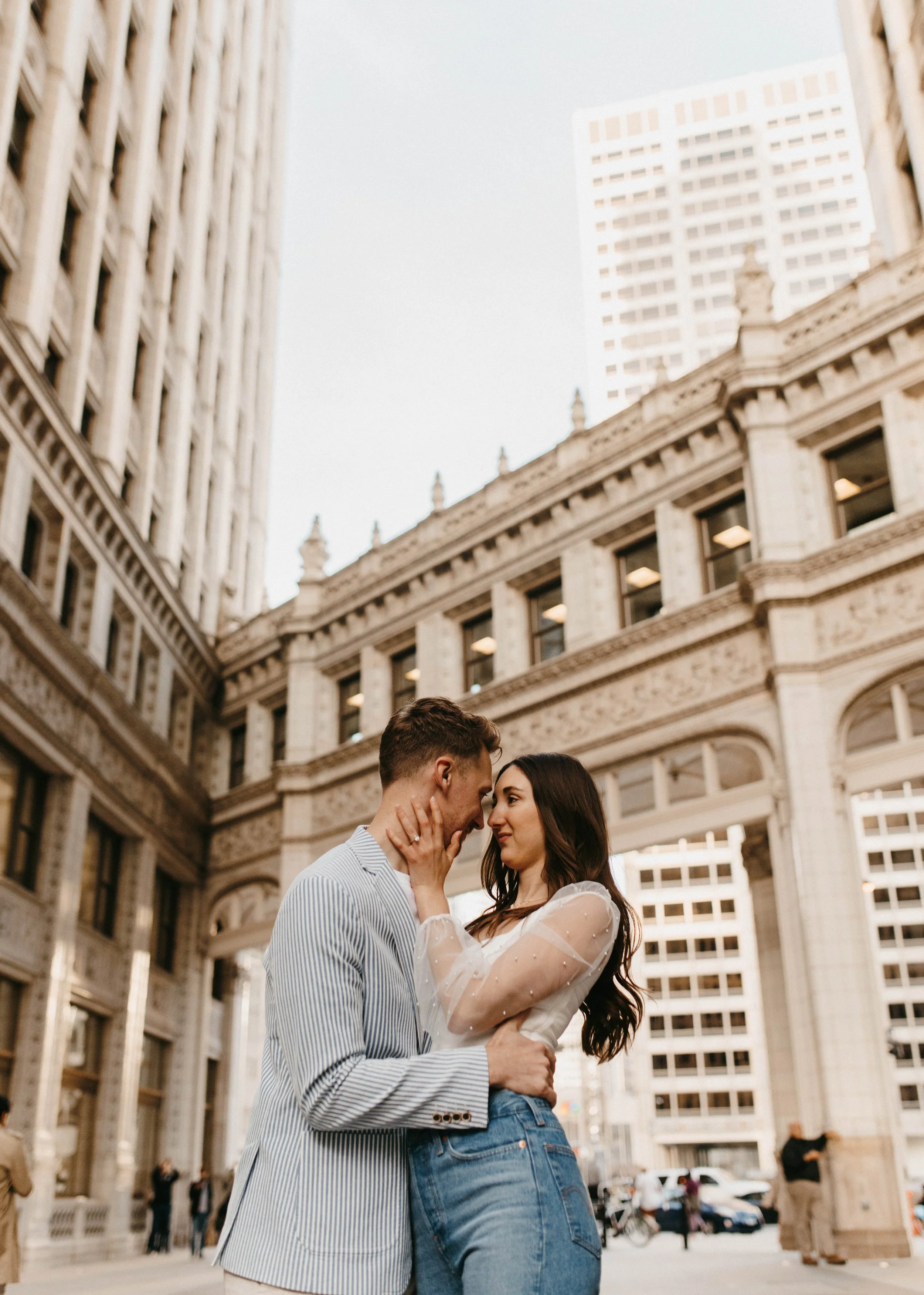 A couple embracing on the street in Chicago with historic buildings and skyscrapers in the background.