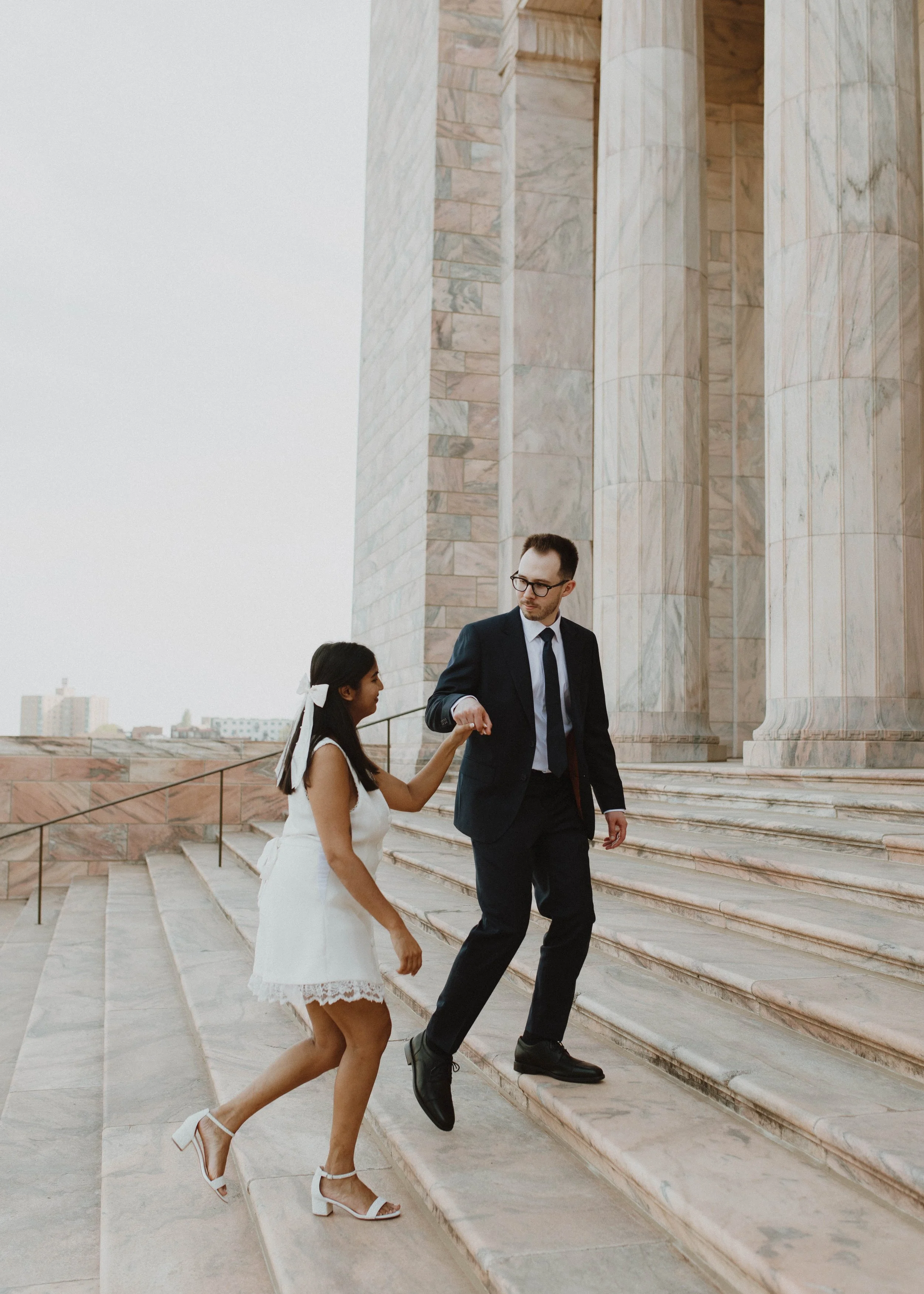 A man in a suit helping a young girl in a white dress down the marble steps outside the Joslyn Art Museum.