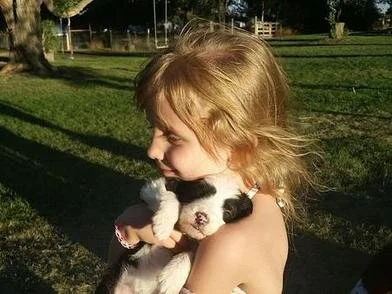 A young child holding a small puppy in a park on a sunny day.