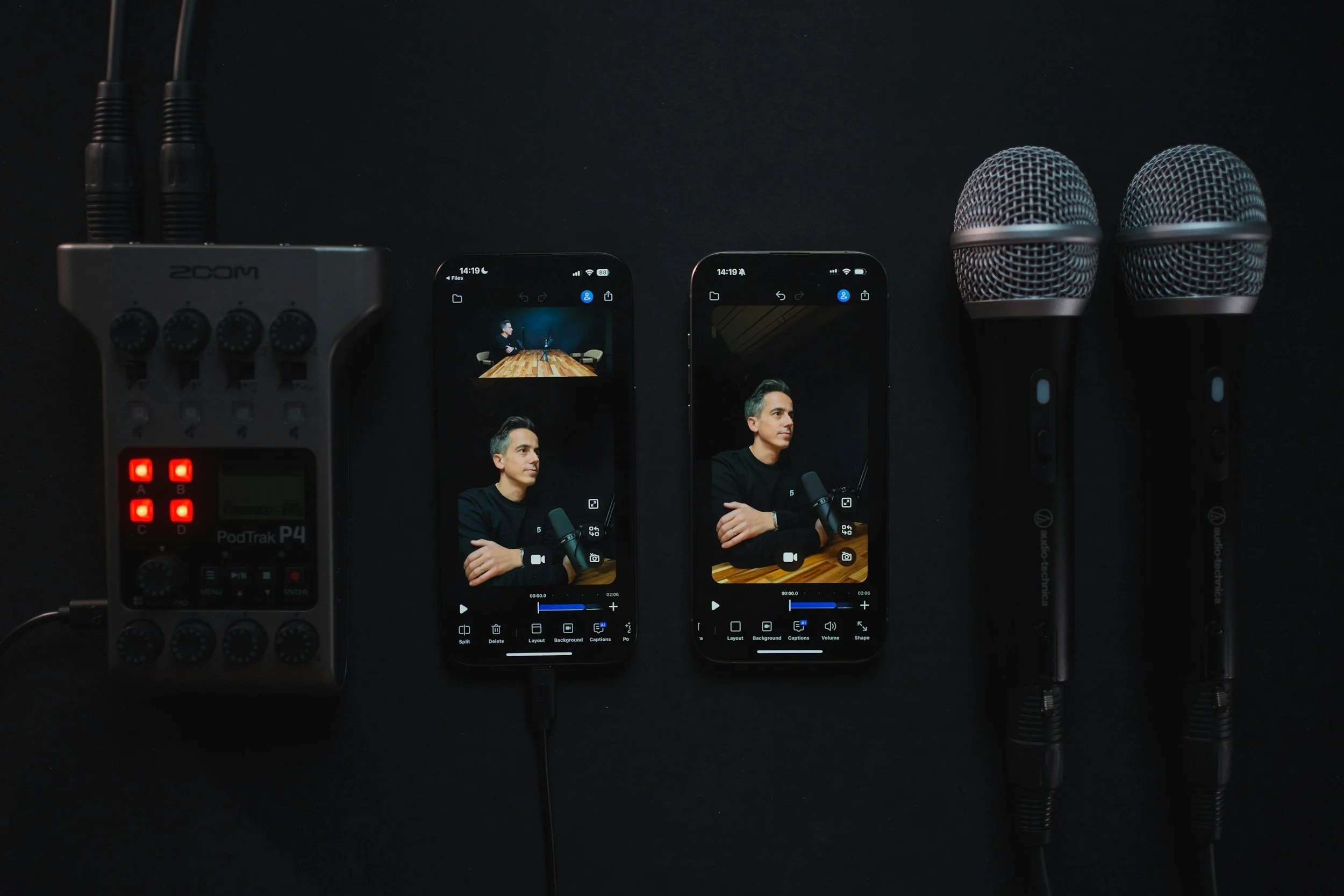 Two smartphones showing a man in a black shirt with crossed arms in a recording studio, flanked by two microphones, a recording device, and cables on a dark surface.