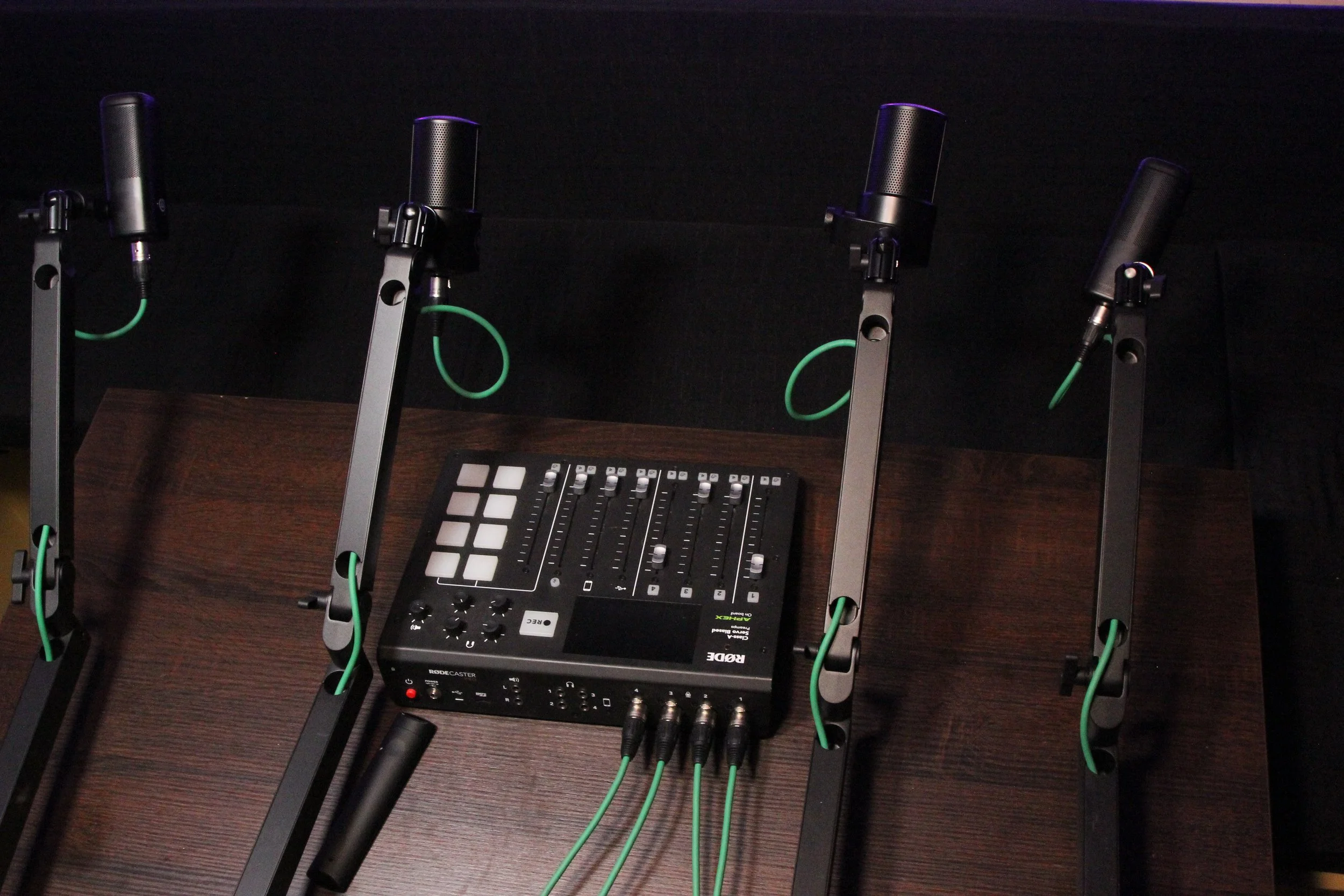 A podcast audio mixing console connected to four microphones on adjustable stands on a wooden table.
