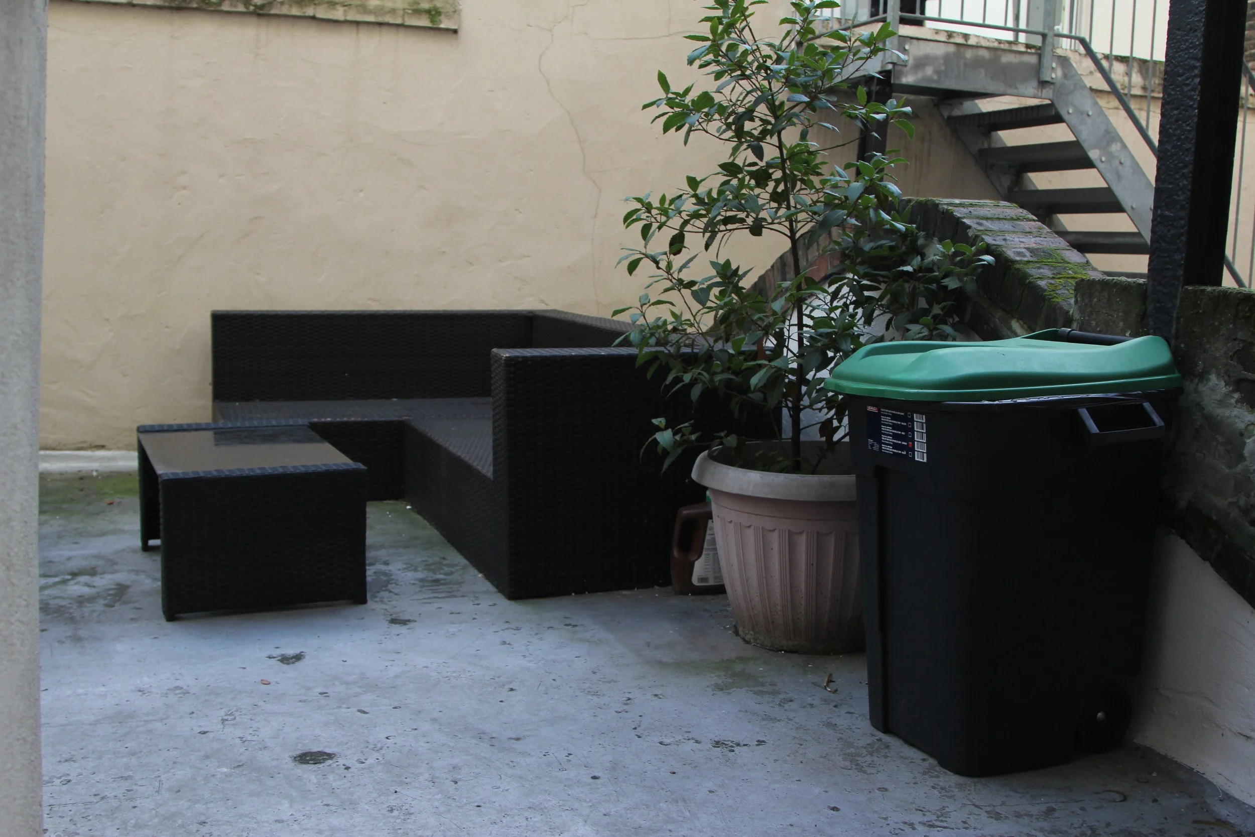 Outdoor patio at a podcast studio in London with black wicker furniture, a potted plant, and a green-topped trash bin.