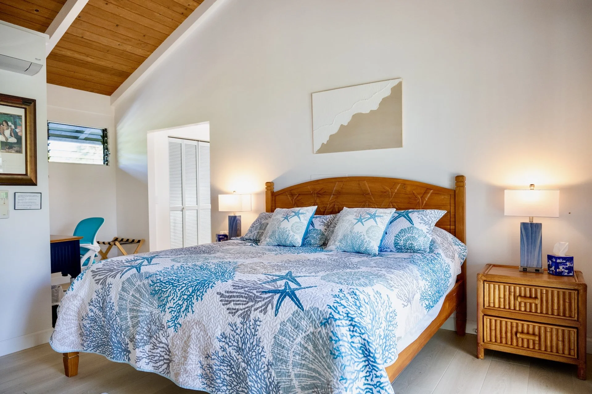 A bedroom with beige walls, a wooden bed frame, and starfish-themed bedding. Two lamps on wooden nightstands and framed artwork on the wall.
