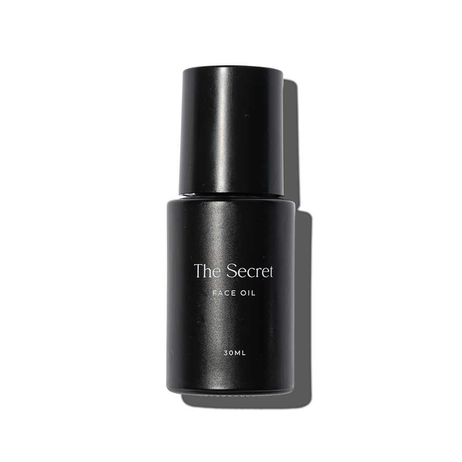 A black bottle of face oil labeled 'The Secret' with a black cap and white text, containing 30ml, against a black background.