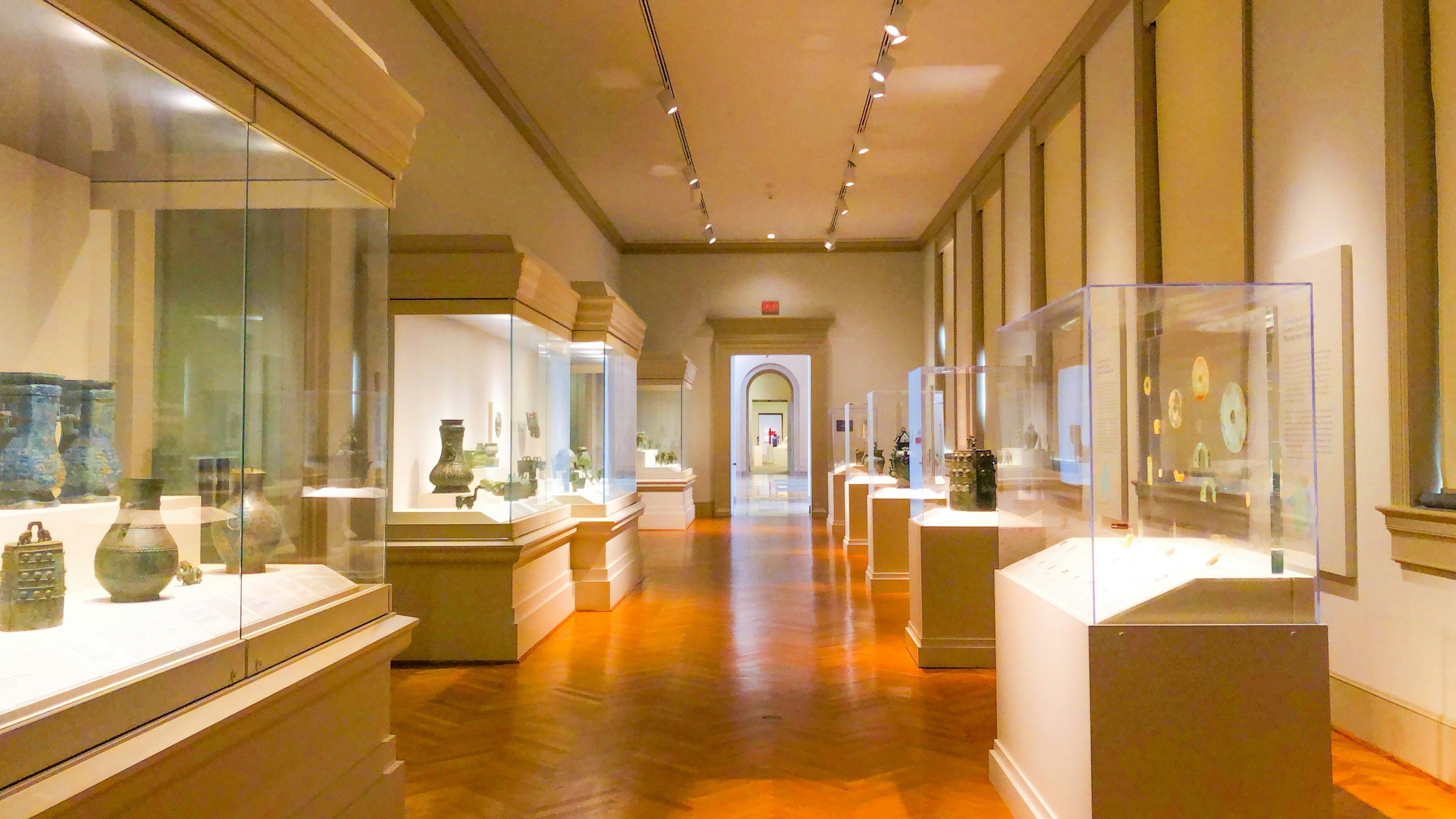 Museum gallery with glass display cases showcasing artifacts on wooden flooring.