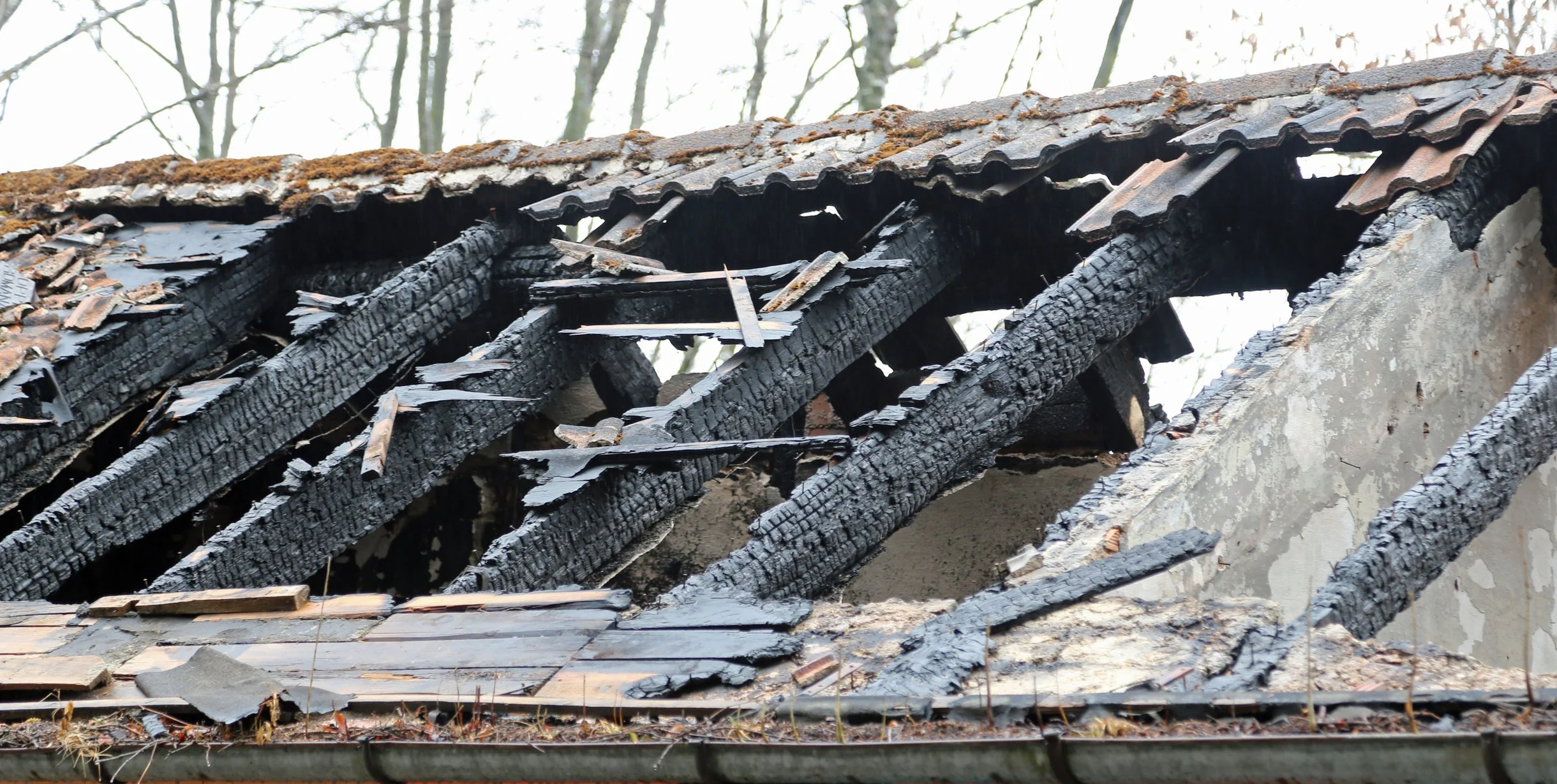 Burnt roof structure with charred wooden beams and damaged tiles.