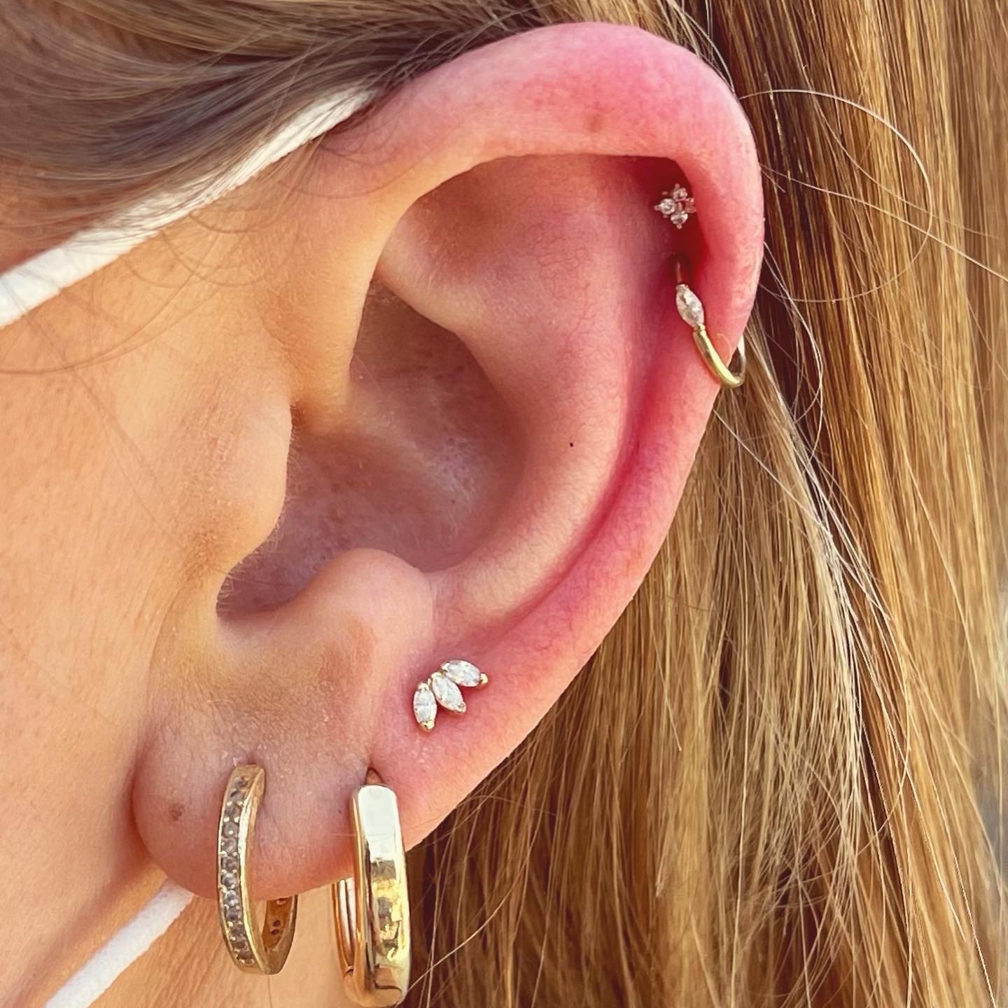 Close-up of an ear with multiple earrings, including gold hoops and a stud