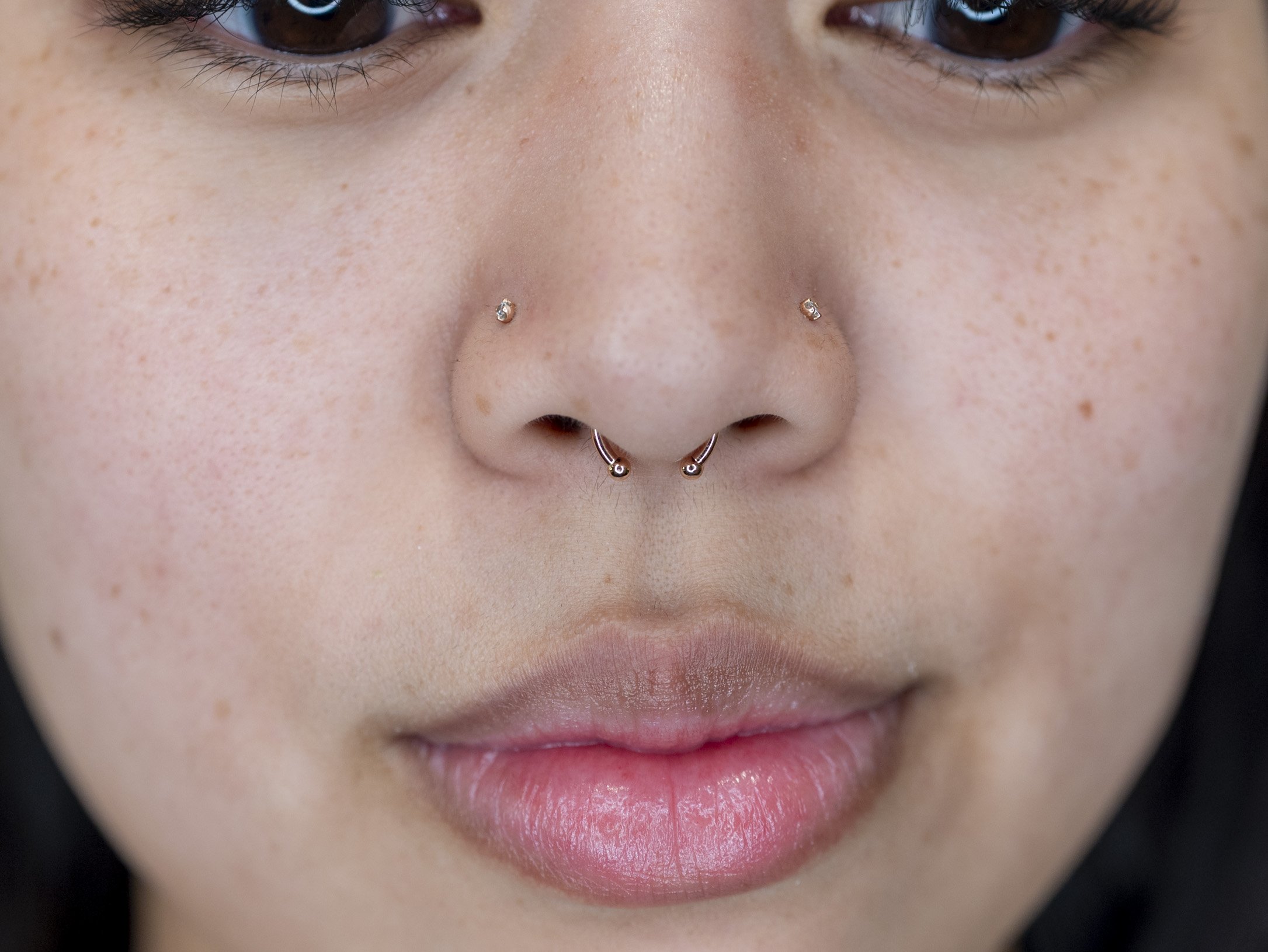 Close-up of a person's nose with a septum ring and two nostril piercings.