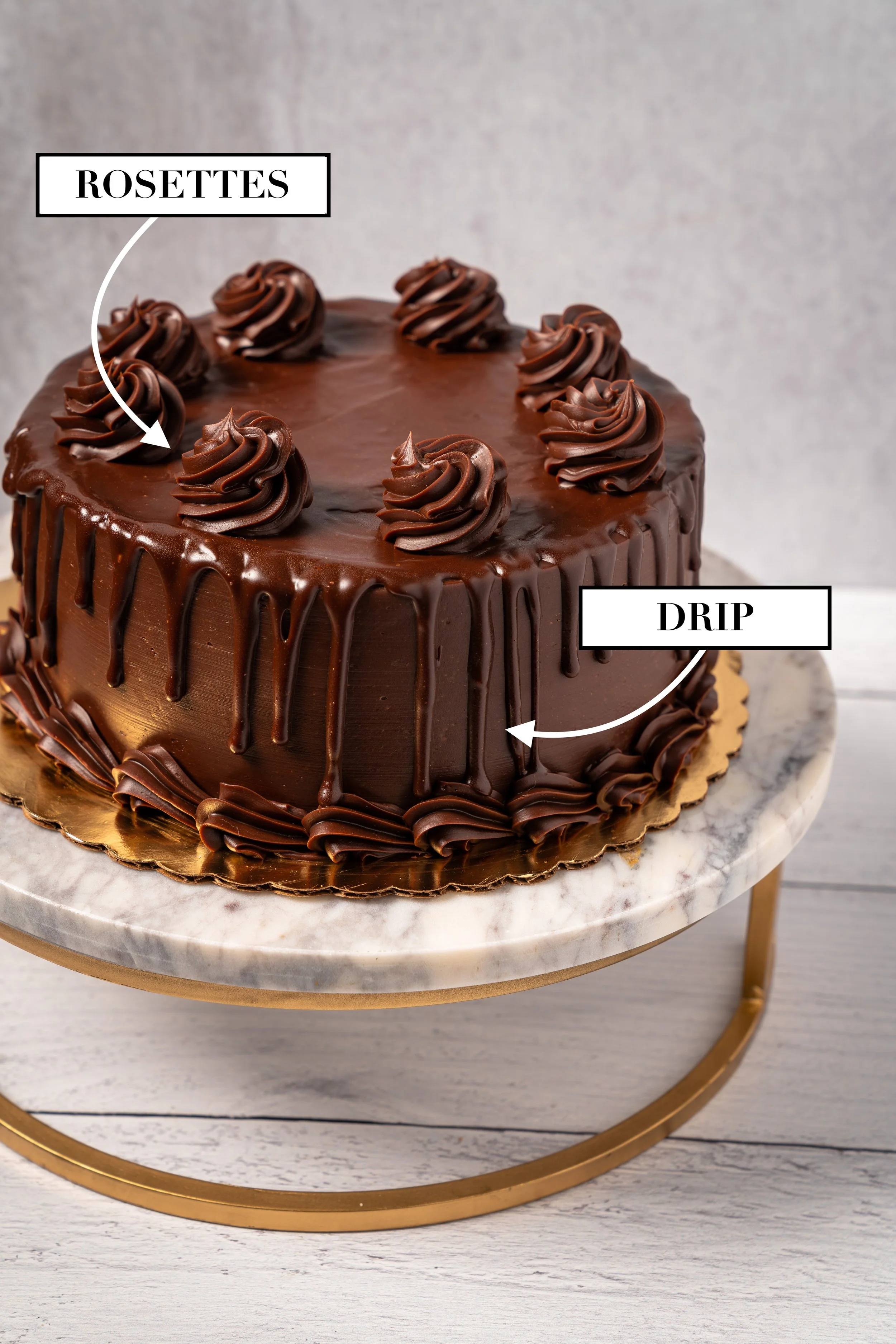 Chocolate cake with rosettes on top and a chocolate drip on the sides, sitting on a marble cake stand.