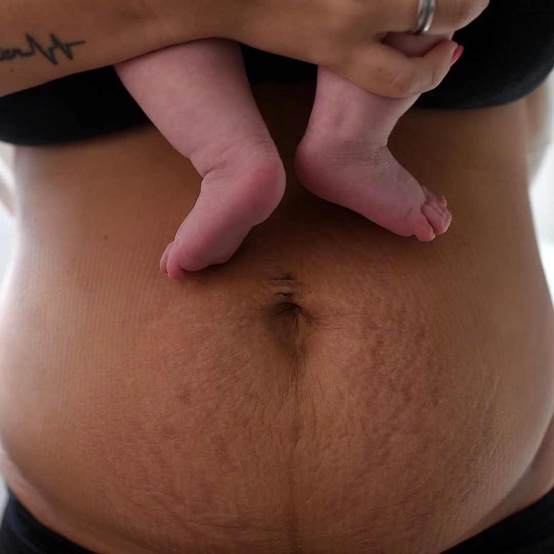 Woman showing postpartum belly while holding baby