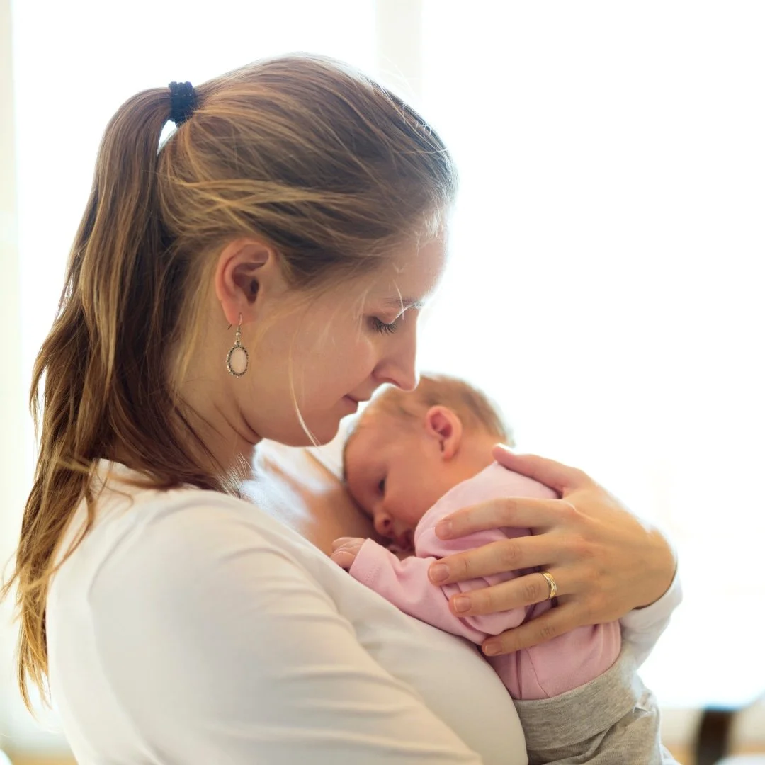 Woman in white holding a sleeping baby in pink